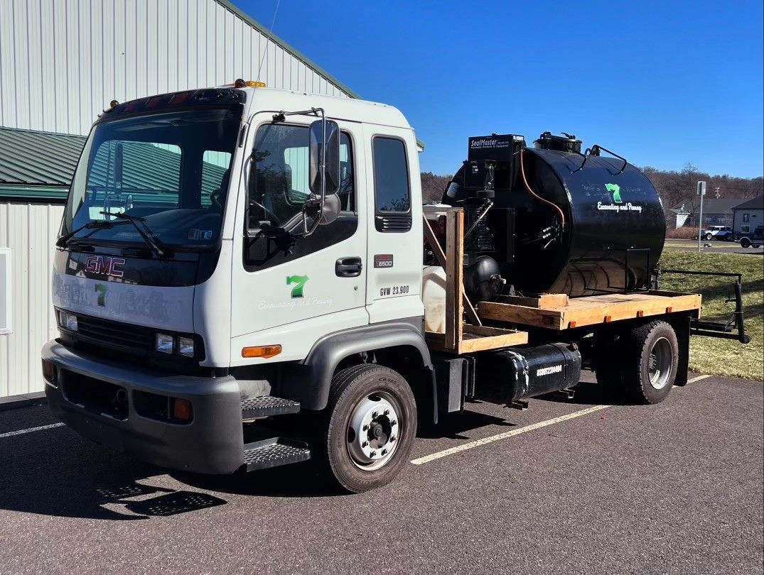 A white cab-over truck with a black cylindrical tank on its flatbed parked in a paved lot on a sunny day.