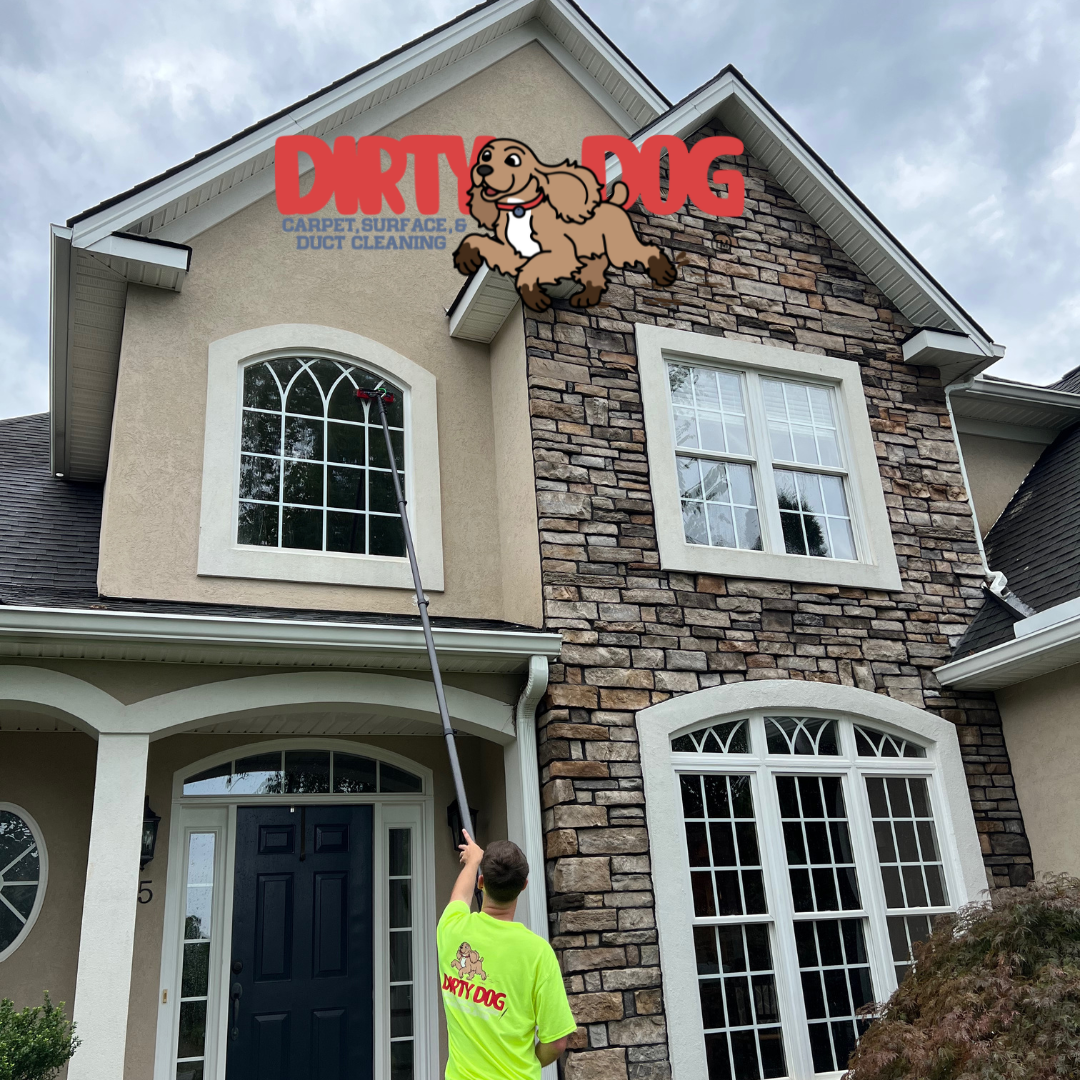 Man washing a house's windows with a long-handled tool.