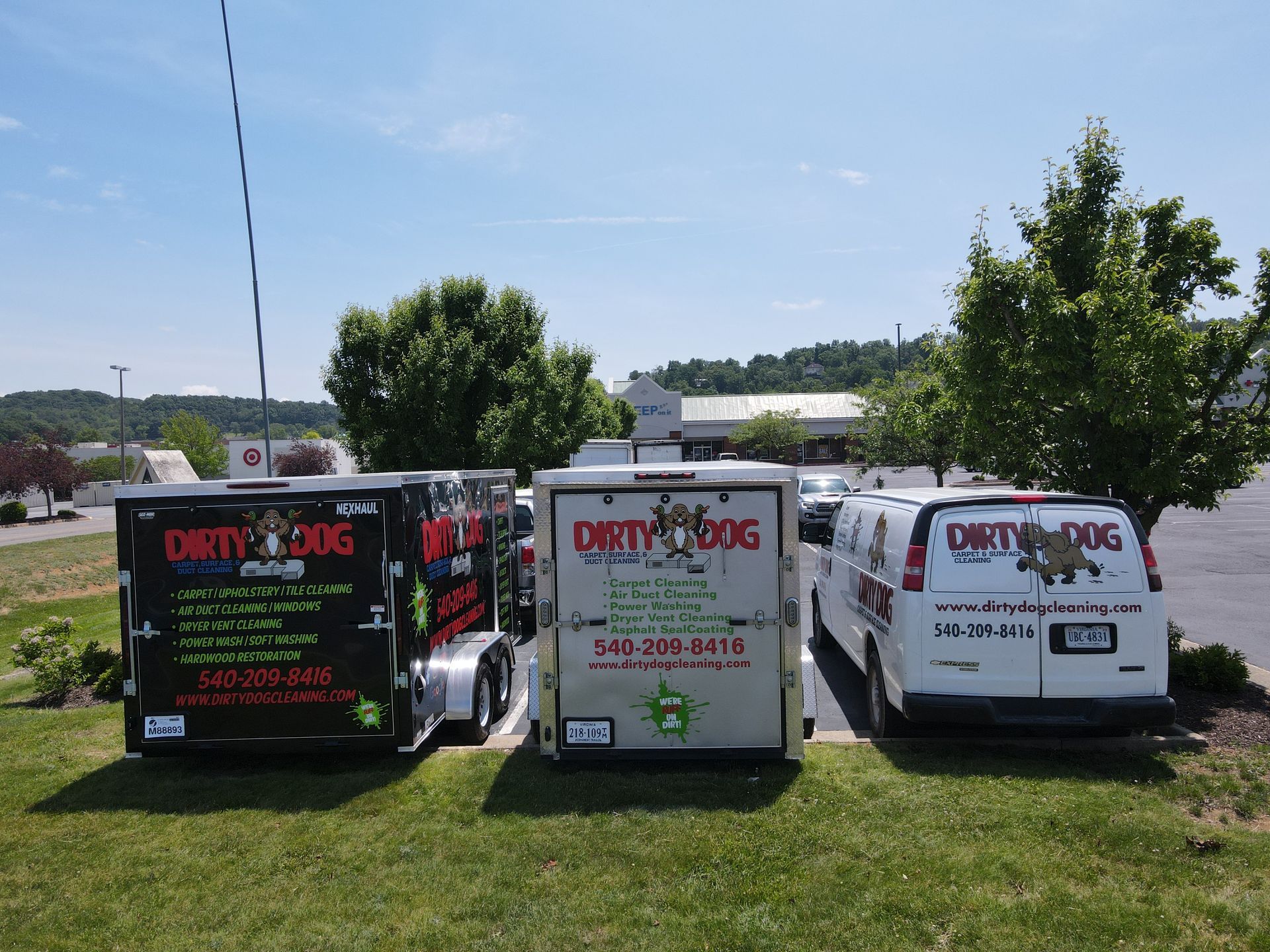 Three vehicles with Dirty Dog logo parked on grass. Trailers and a van in a parking lot on a sunny day.