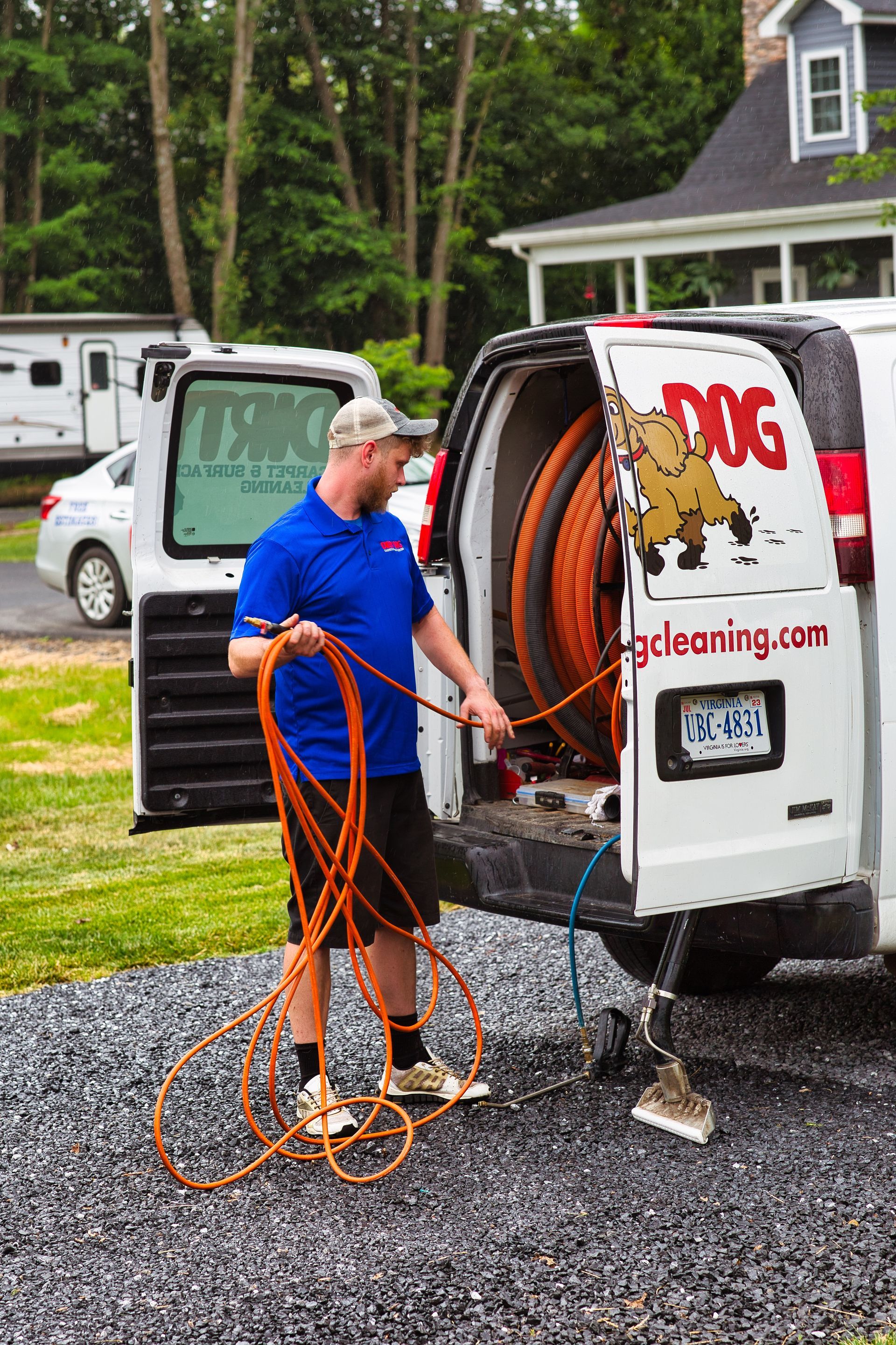 Man with blue shirt uncoils hose from a van, preparing for carpet cleaning.