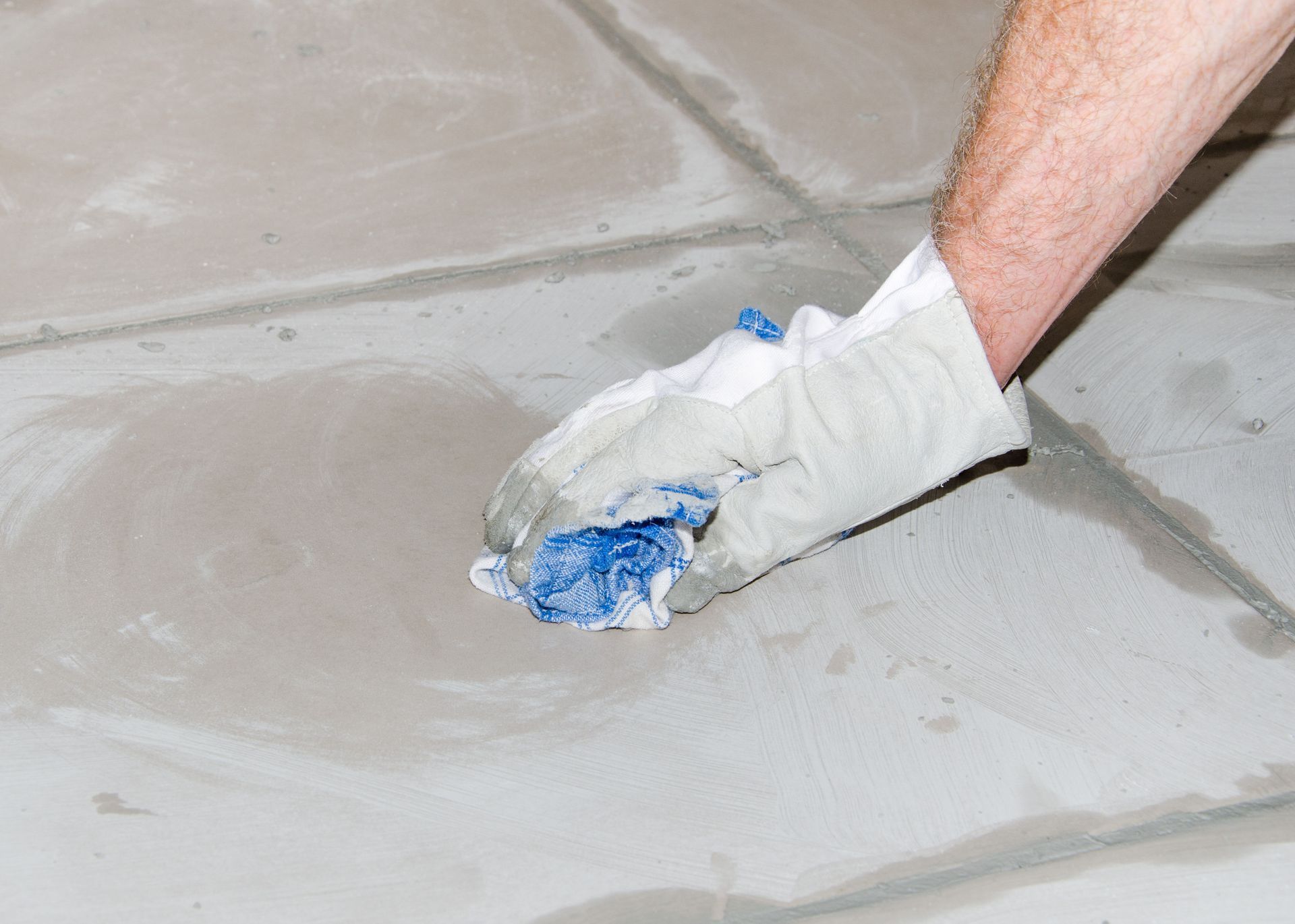 Gloved hand wiping grout between light-colored tiles, blue smear on rag.