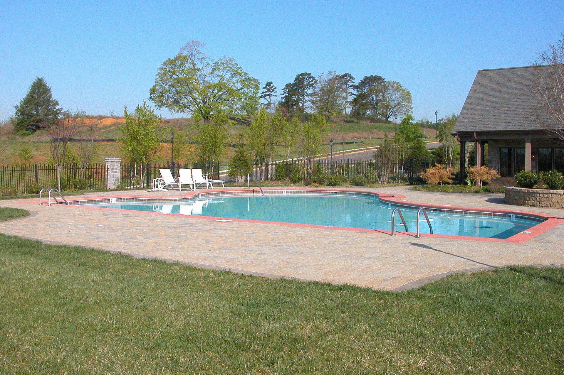 Outdoor swimming pool with blue water, red deck, grassy lawn, and a house in the background