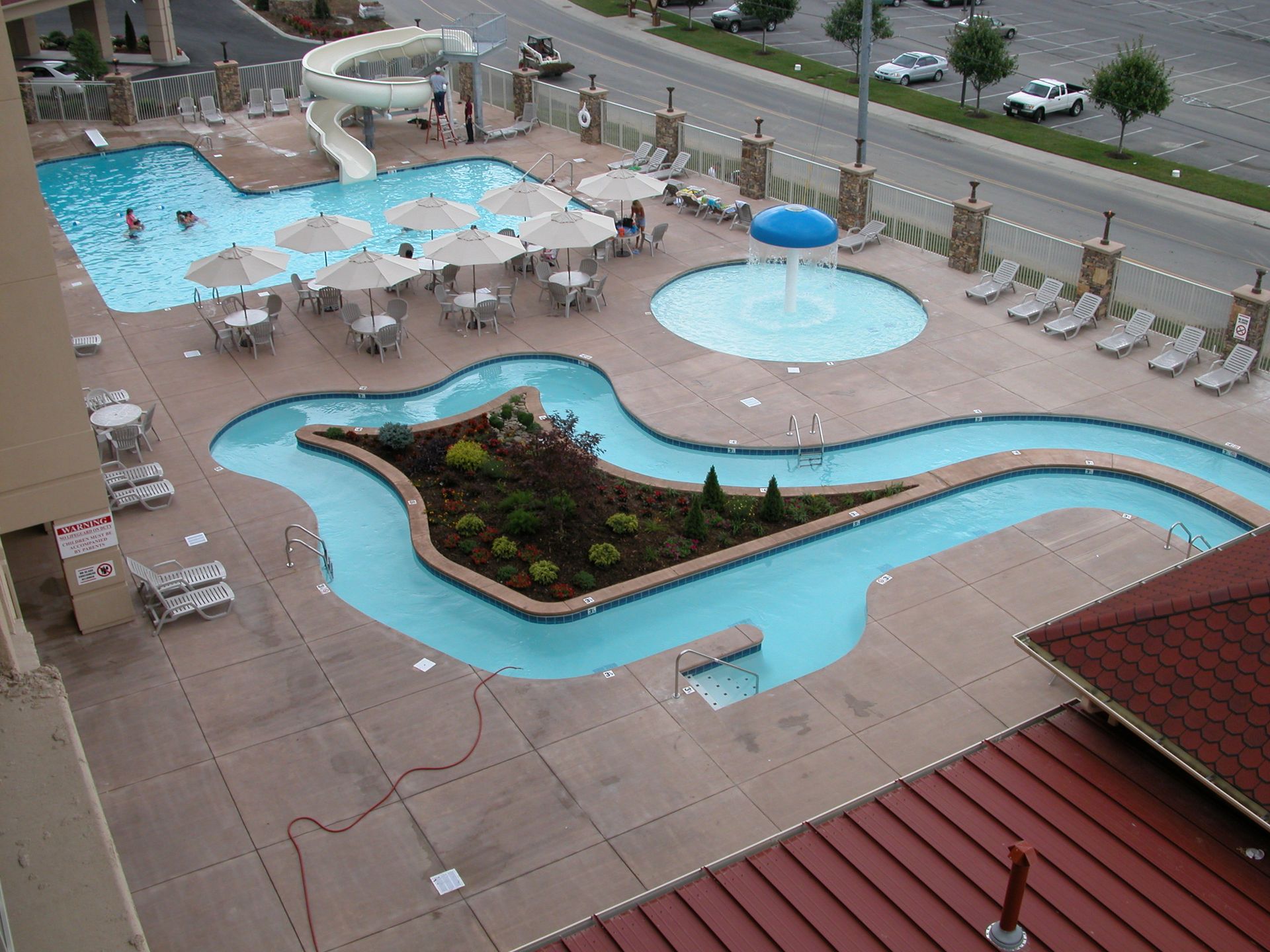 Overhead view of a hotel pool deck with winding blue pools, lounge chairs, and a road nearby