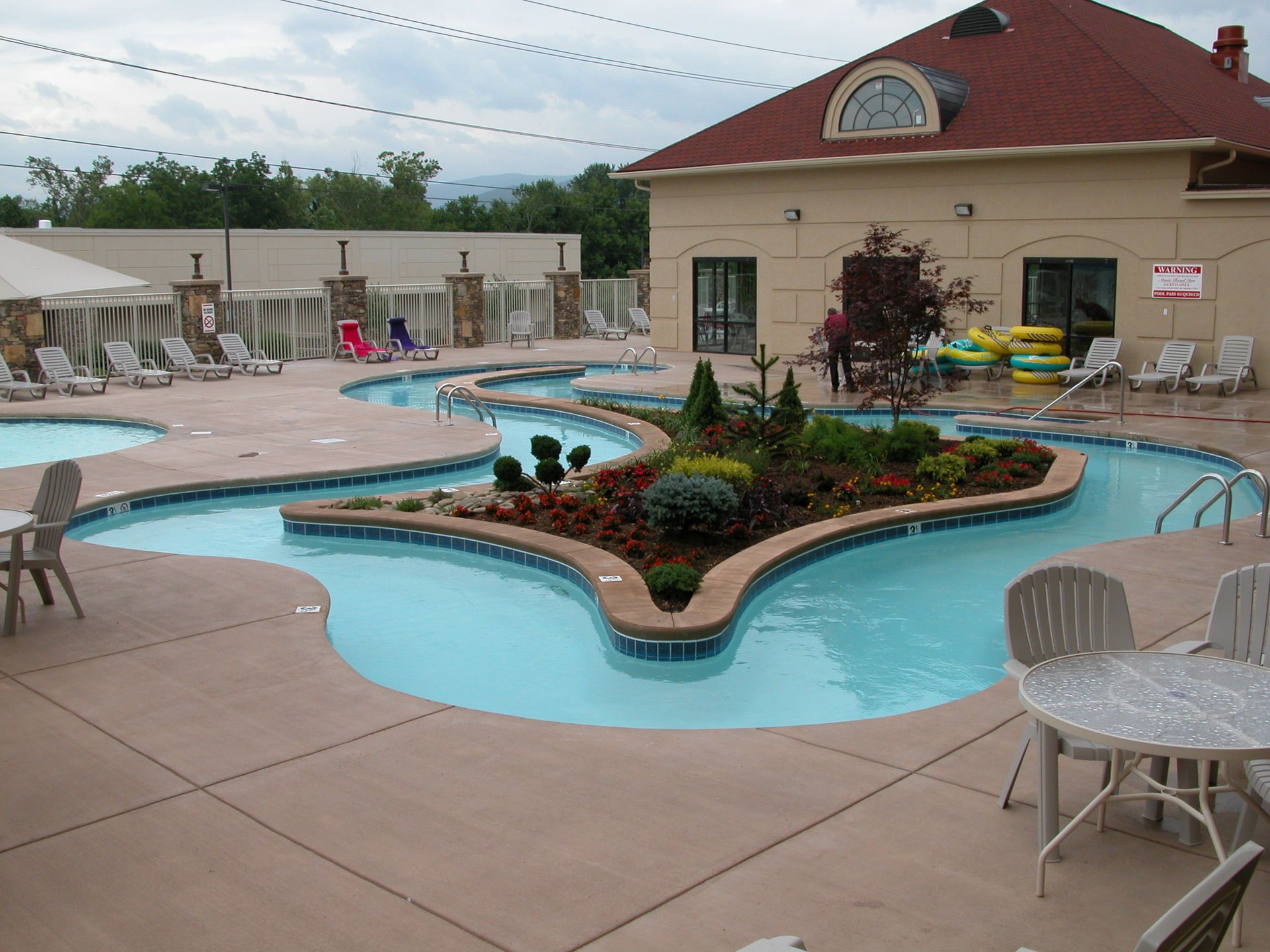 Outdoor pool with a curved island planter beside a beige building and lounge chairs on the deck