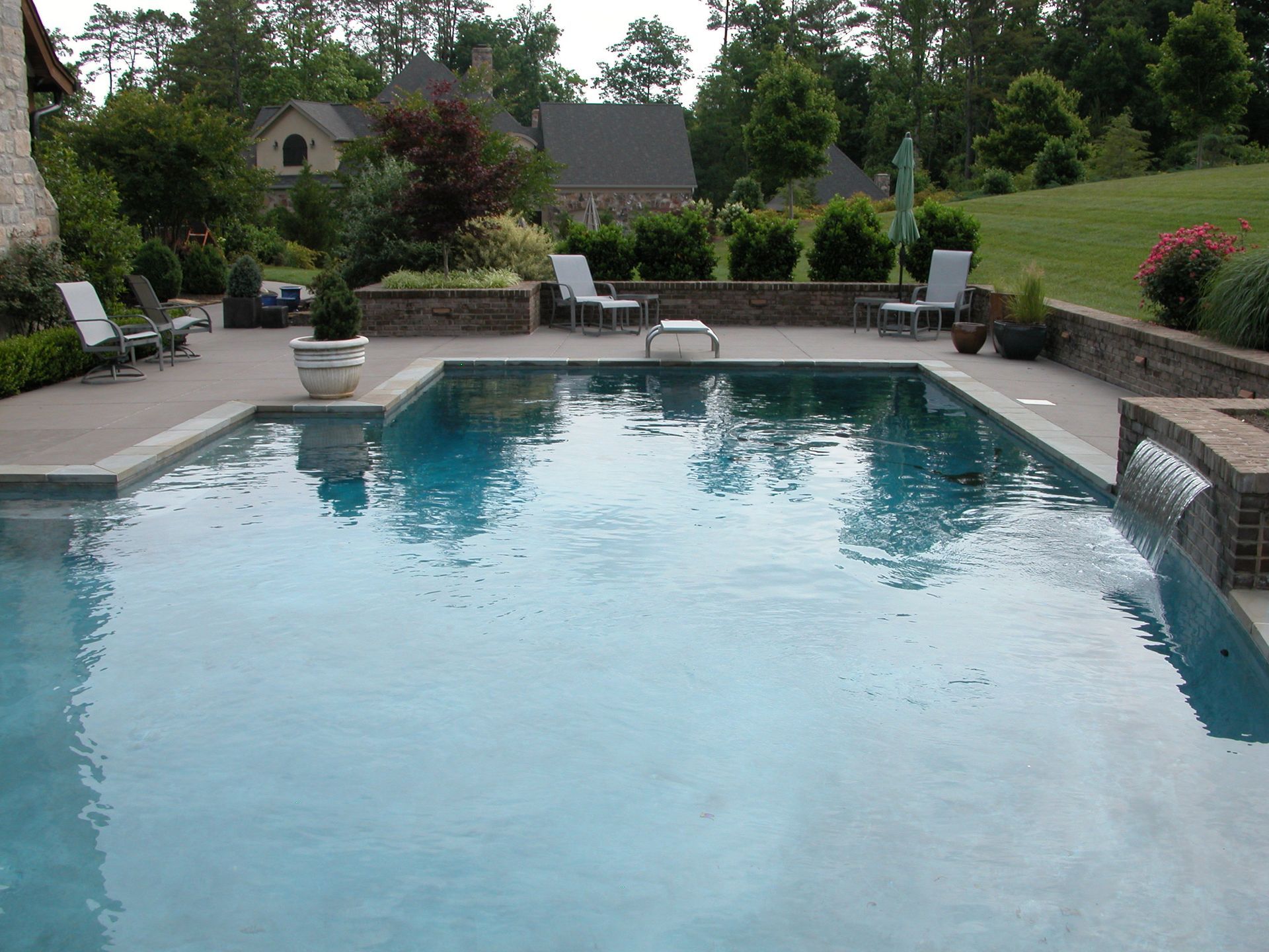 Backyard swimming pool with lounge chairs and greenery surrounding it