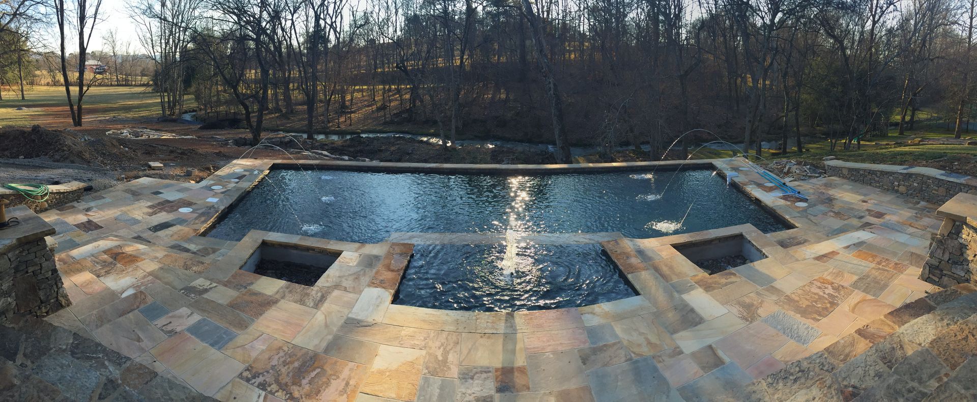 Outdoor stone patio with a central reflecting pool and bare trees in the background