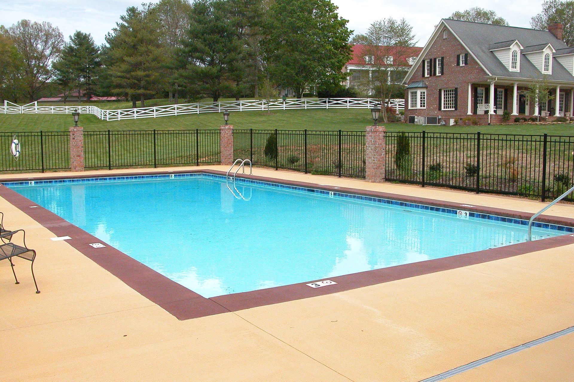 Outdoor swimming pool with blue water beside a brick house and fence