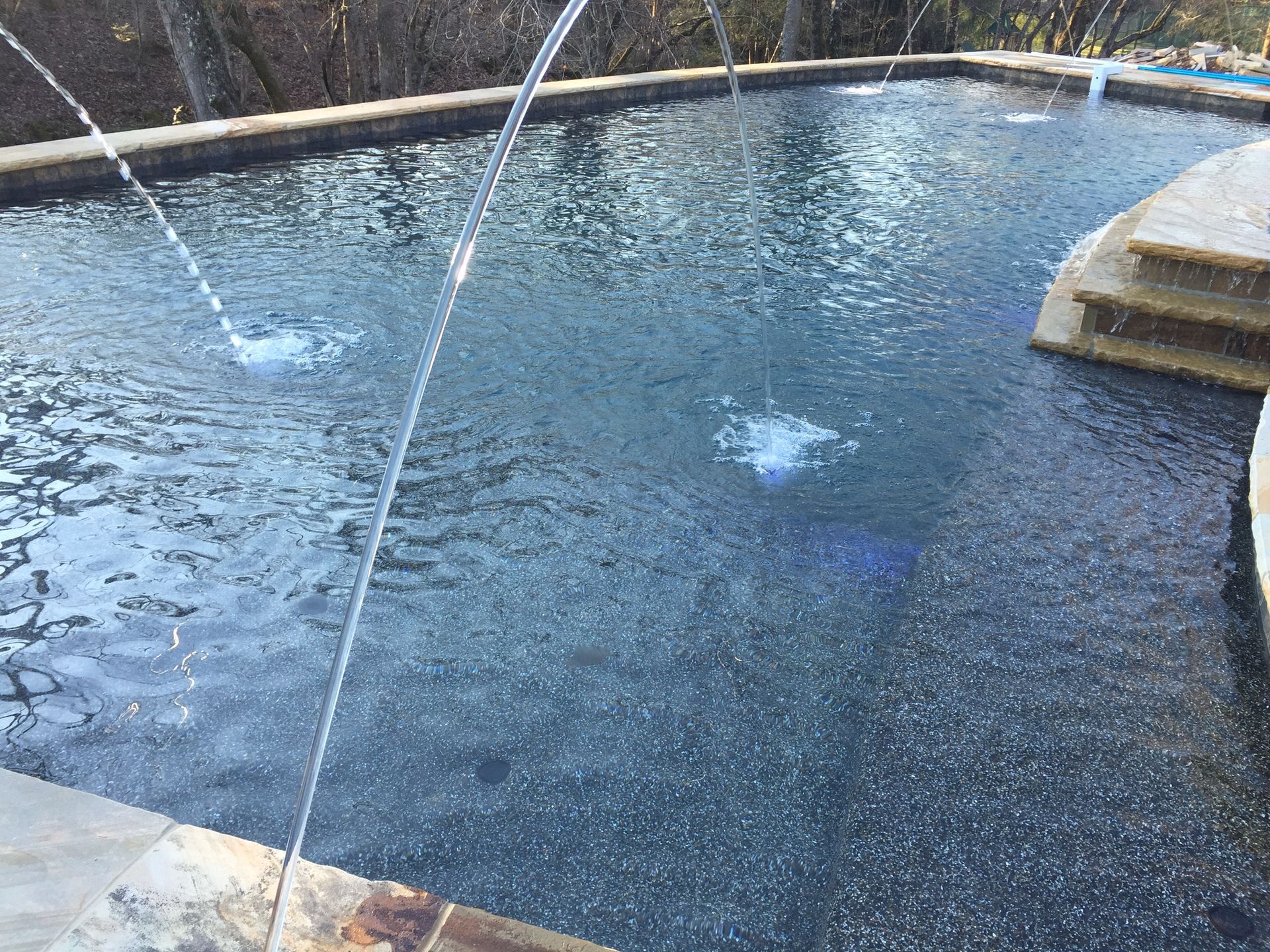 Curved outdoor fountain pool with water jets spraying into a blue, tiled basin