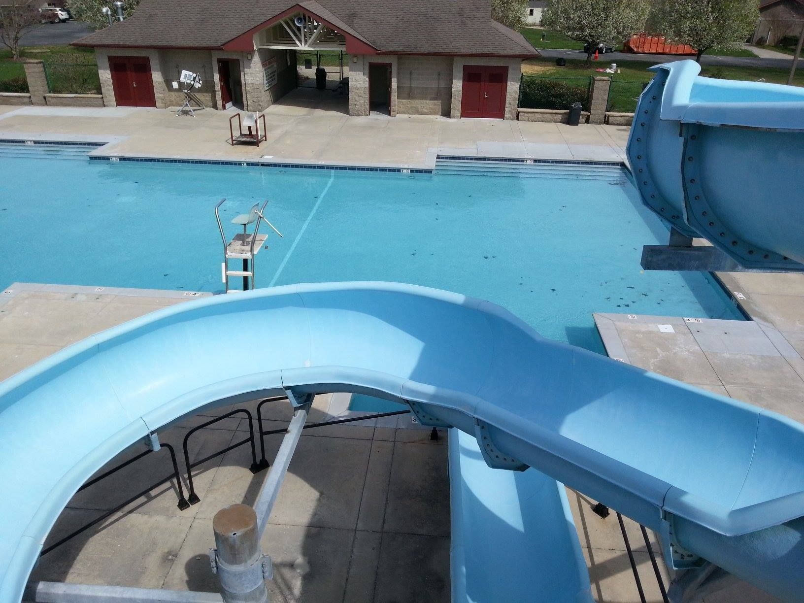 Blue water slide by a swimming pool with a house and deck in the background