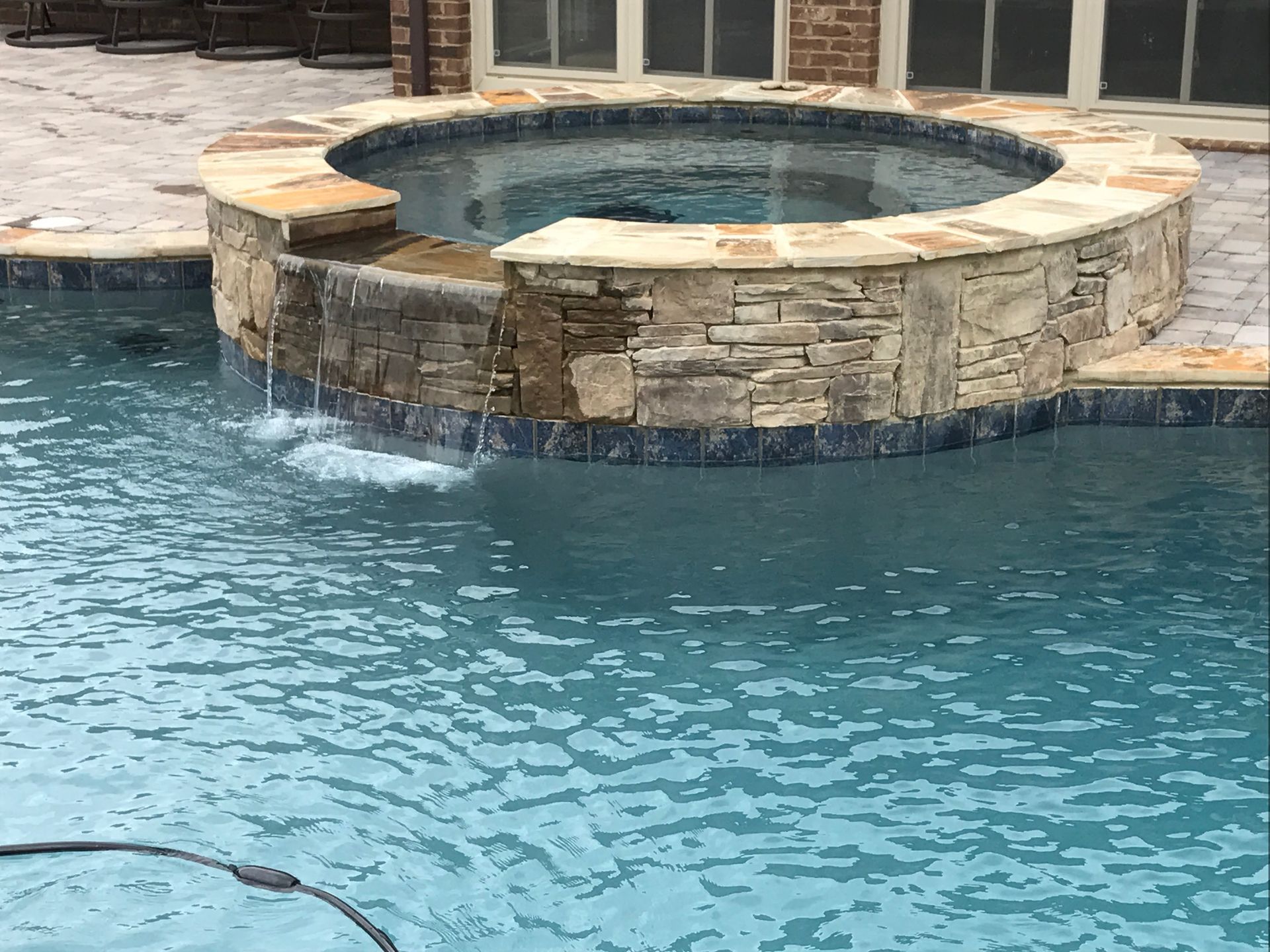 Blue swimming pool with a stone hot tub and tiled patio area