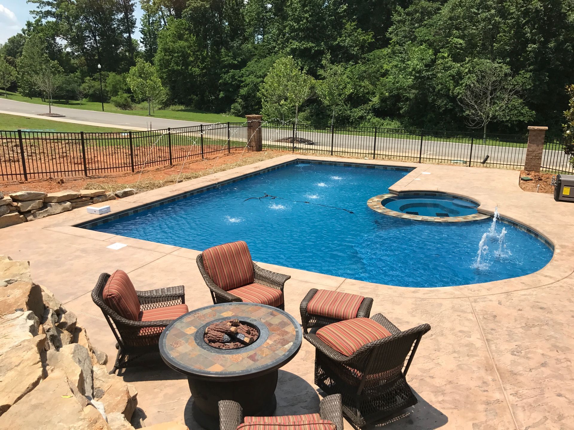 Backyard pool with fire pit seating on a stone patio, blue water, and a built-in hot tub.