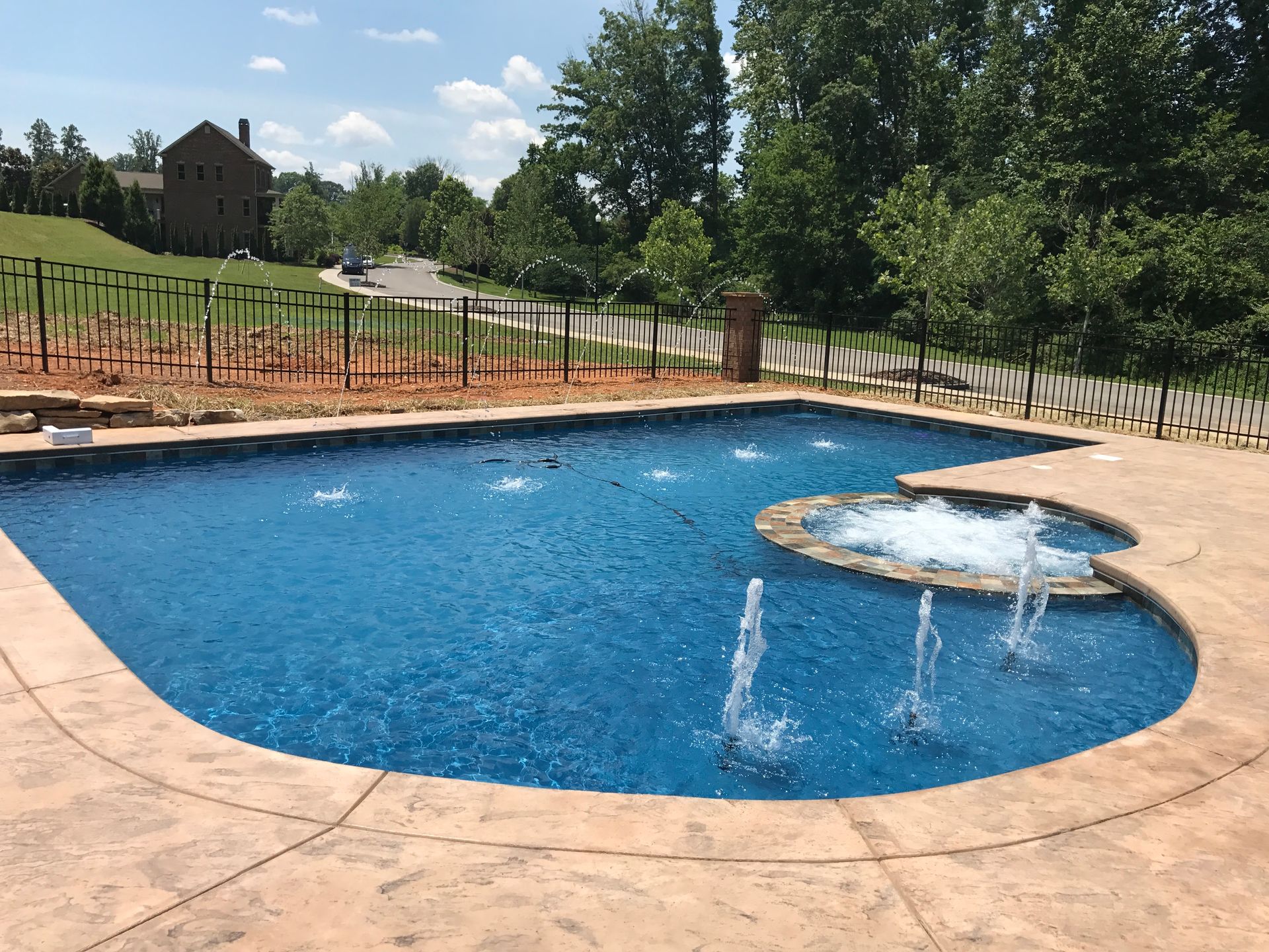 Backyard swimming pool with a shallow splash area, blue water, and tan concrete deck under a sunny sky