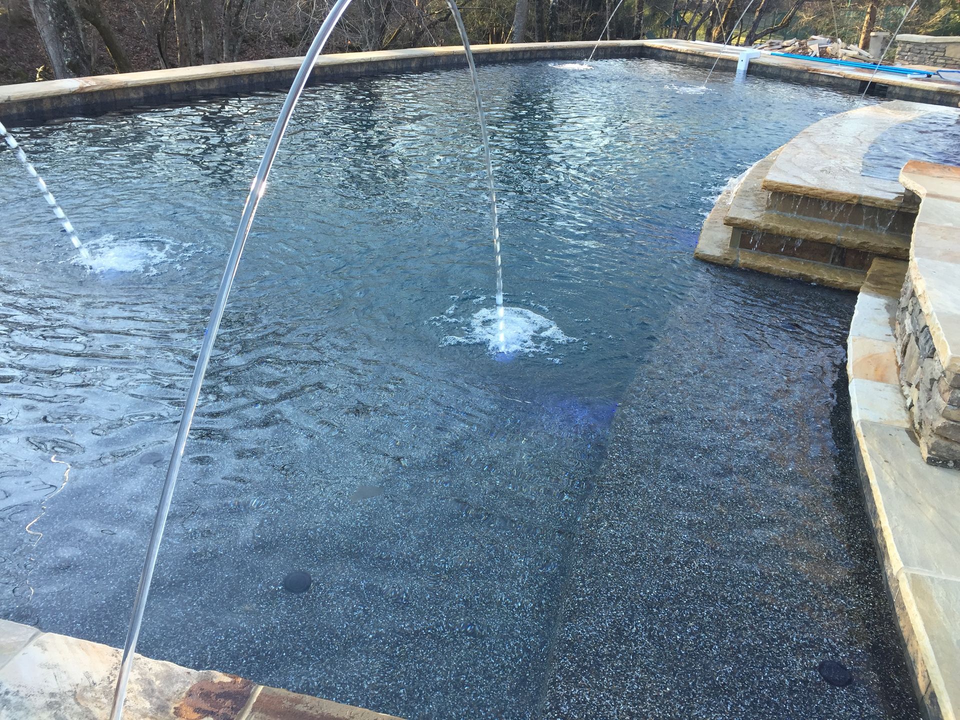Curved backyard pool with bubbling water jets and stone steps along the edge