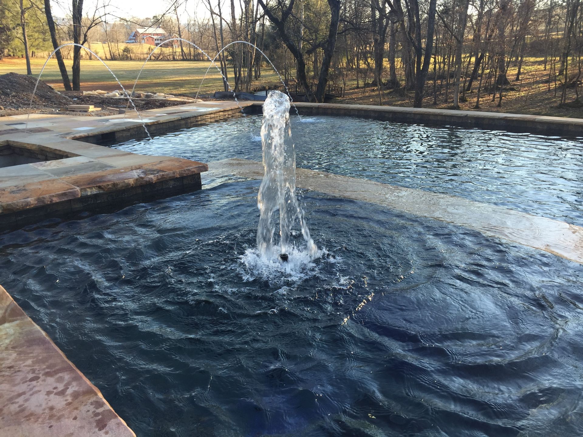 Water fountain spraying in a stone-lined pool in a wooded park.