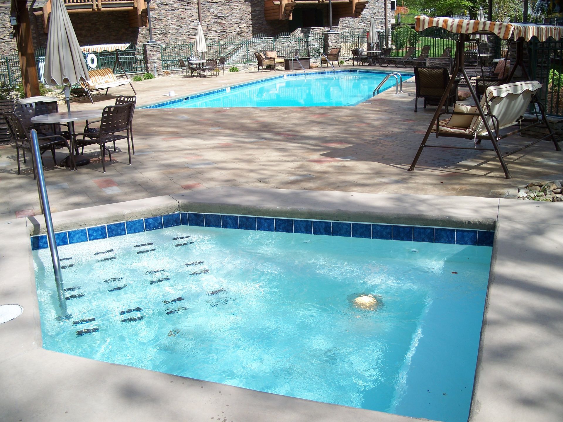 Outdoor resort pool with blue water, stone patio, lounge chairs, and tables under trees