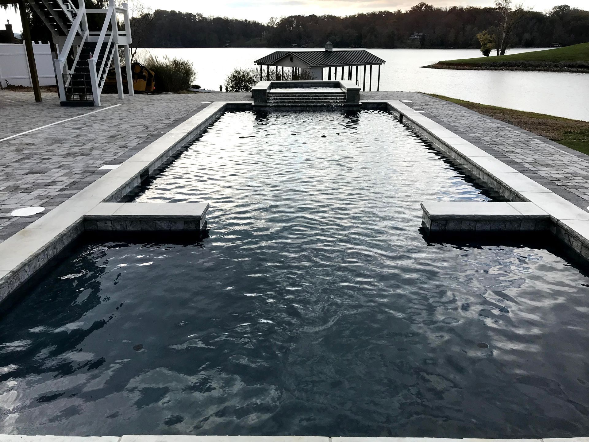 Rectangular outdoor pool with rippling water beside a lake at dusk