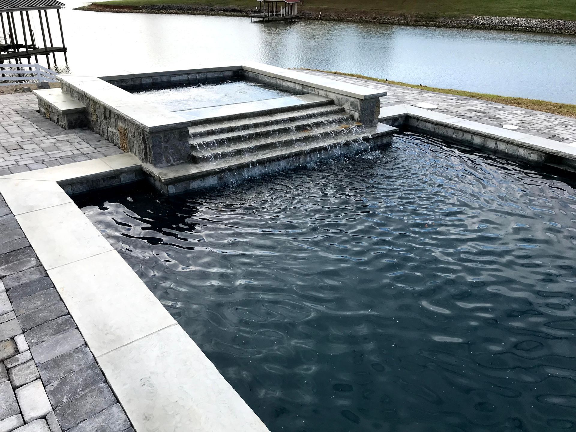 Rectangular outdoor pool with stone steps and a raised spa beside a canal