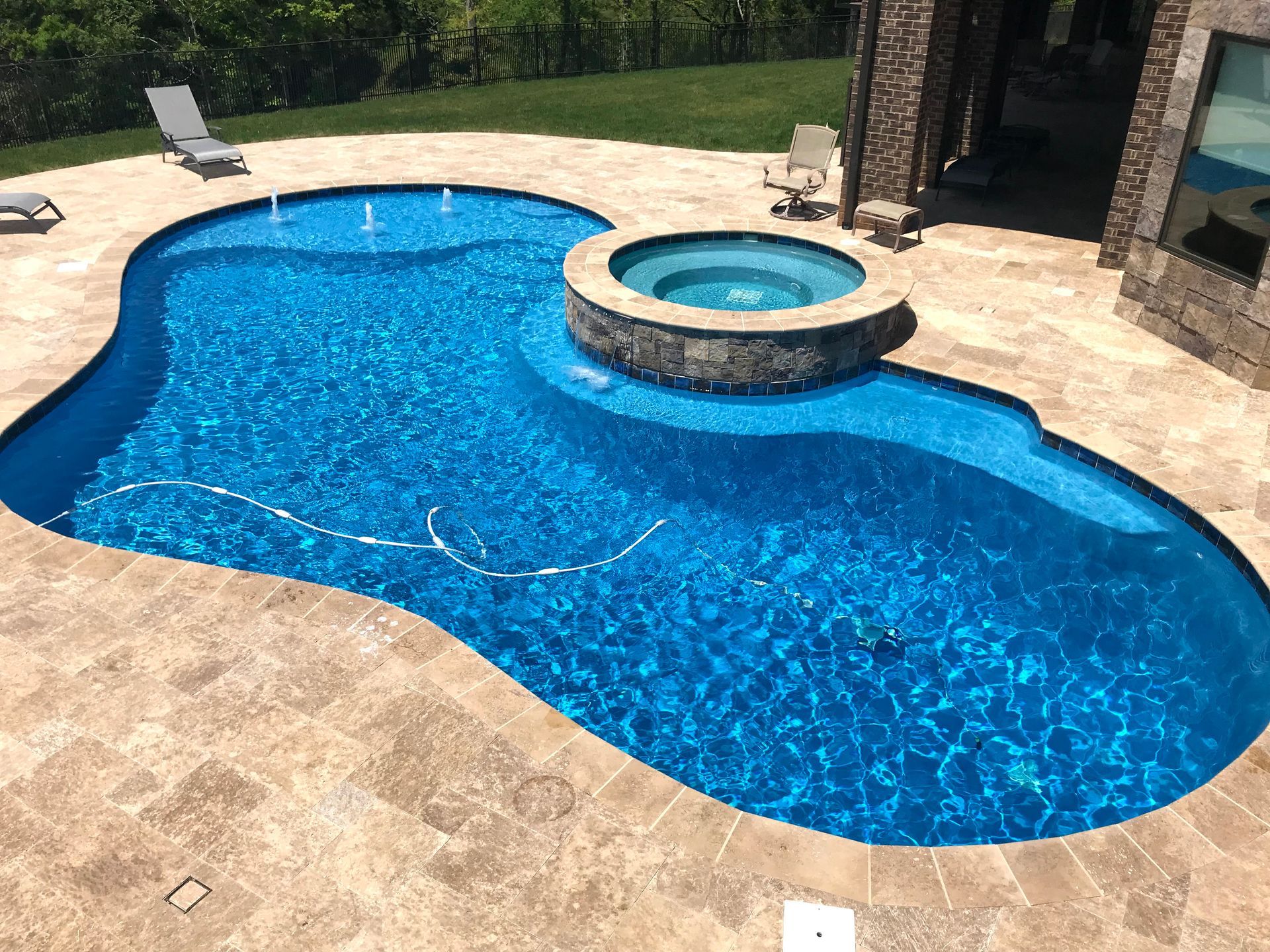 Blue backyard pool with a raised circular hot tub and tan stone patio