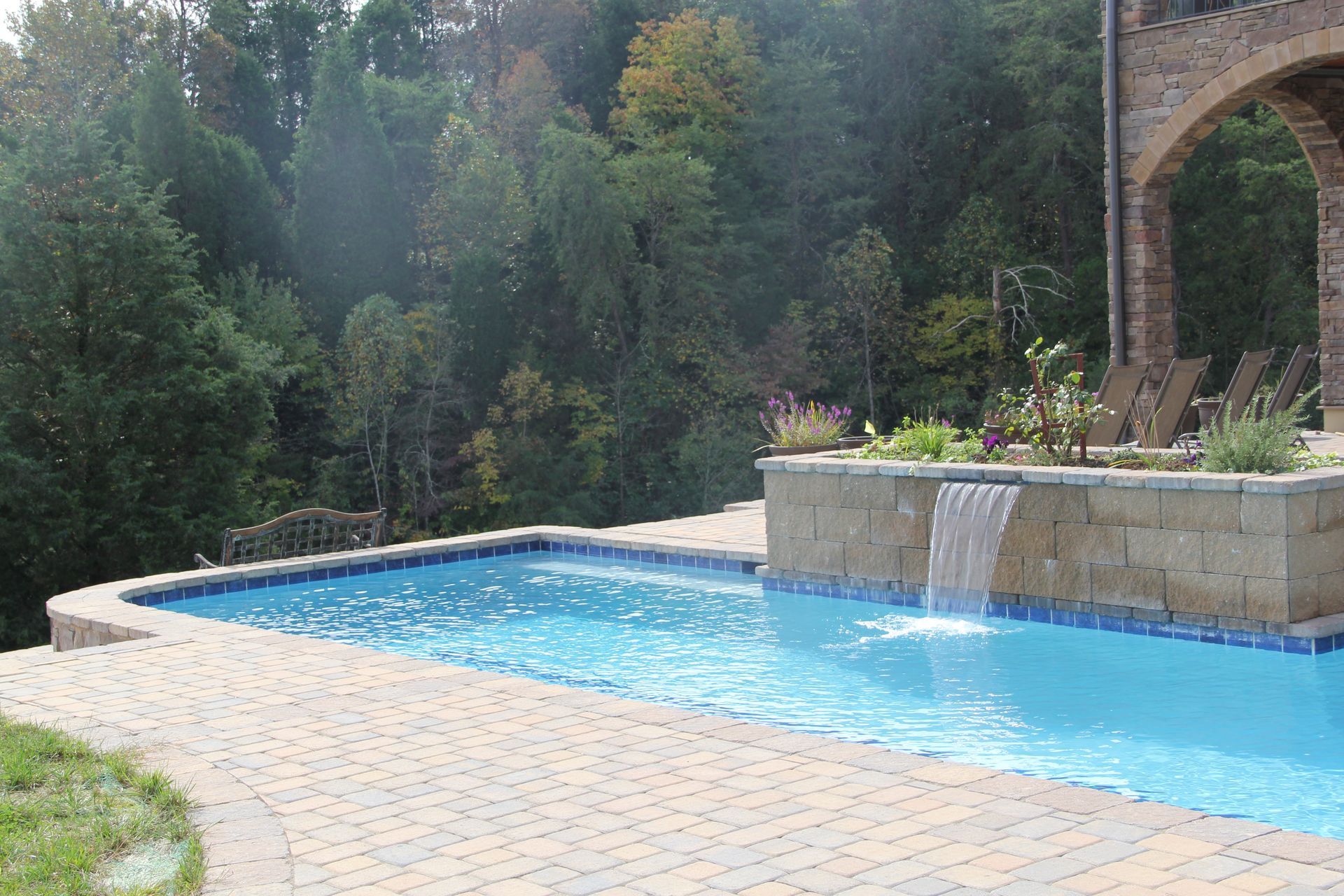 Outdoor swimming pool with bright blue water beside a stone patio and lush wooded hillside