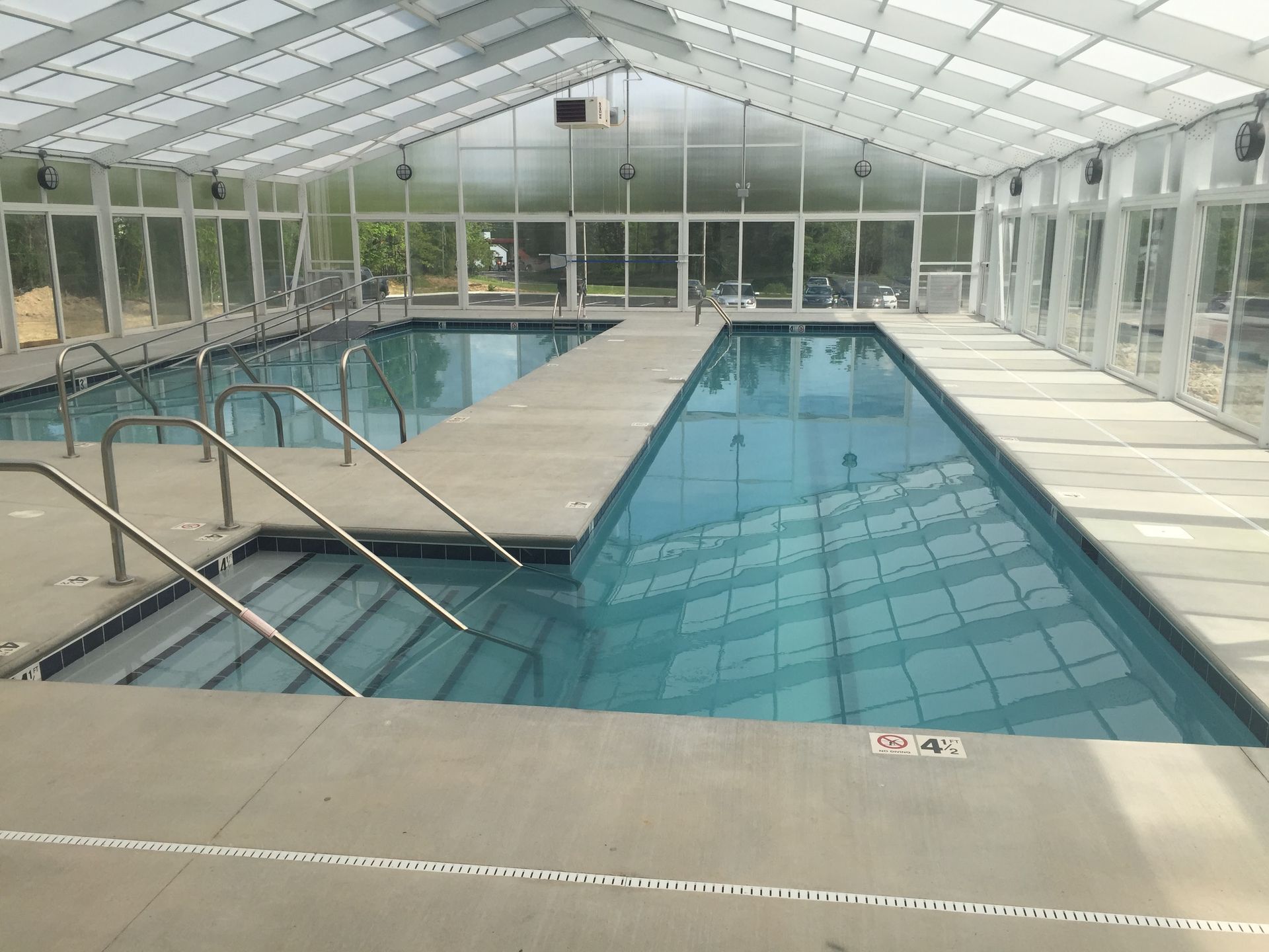 Indoor swimming pool with clear water, white-tiled deck, and a glass-enclosed roof.