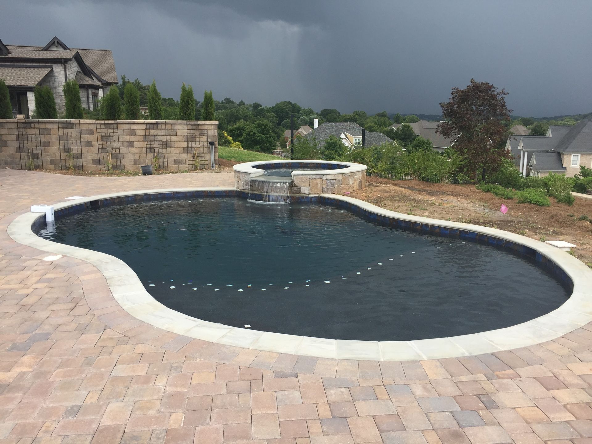 Backyard swimming pool with dark water, stone deck, and stormy sky in the background