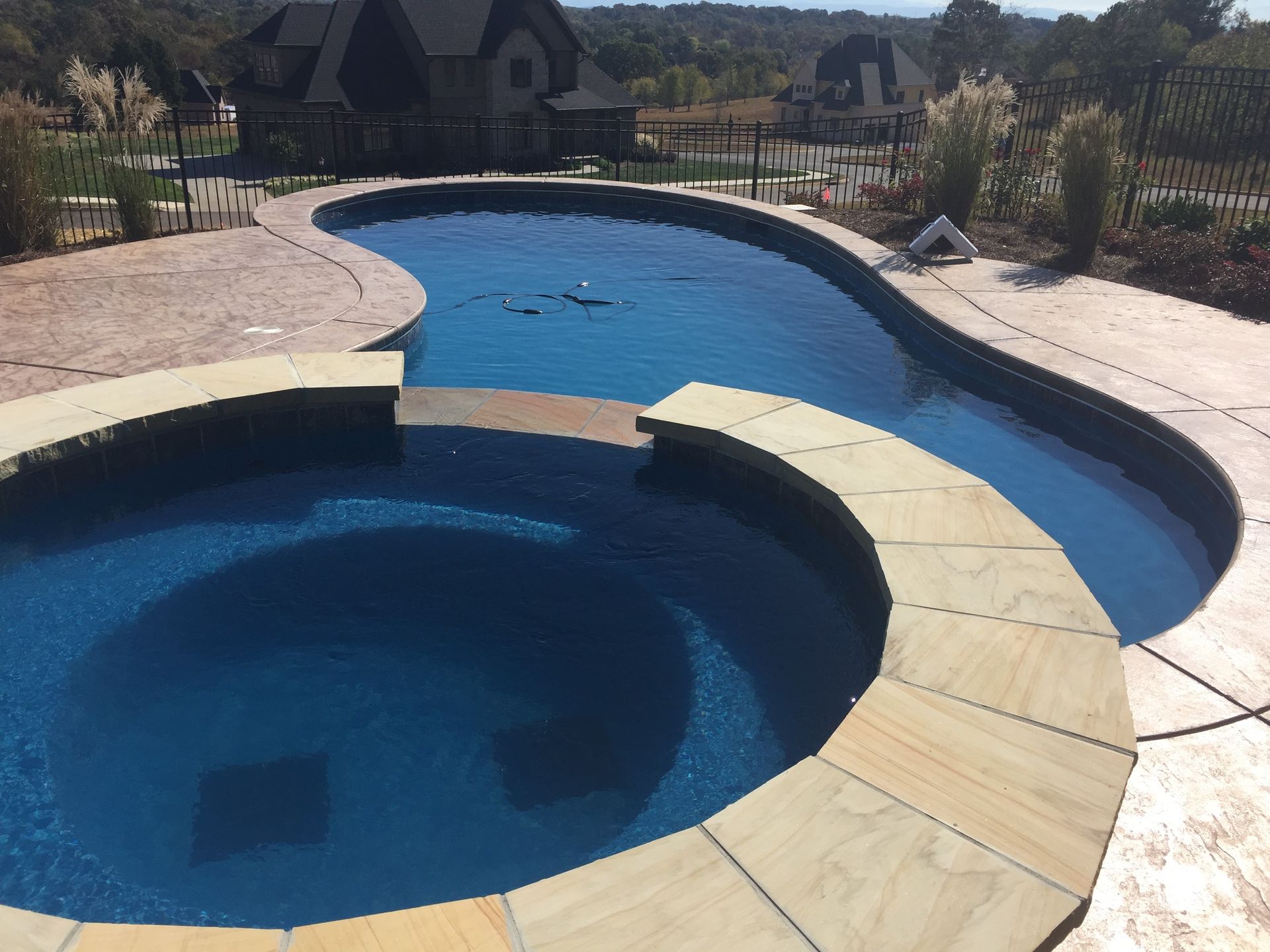 Curved backyard swimming pool with a circular hot tub and stone deck under bright sunlight