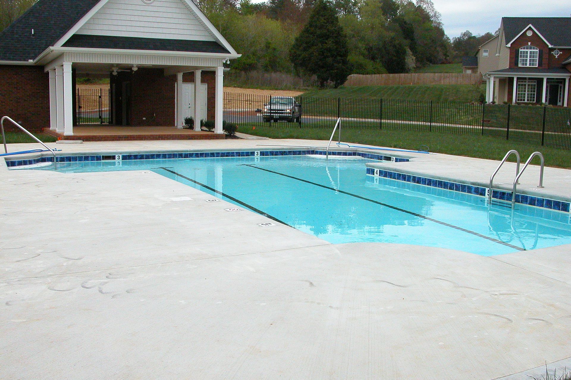 Outdoor swimming pool with bright blue water and a white concrete deck beside a pavilion.