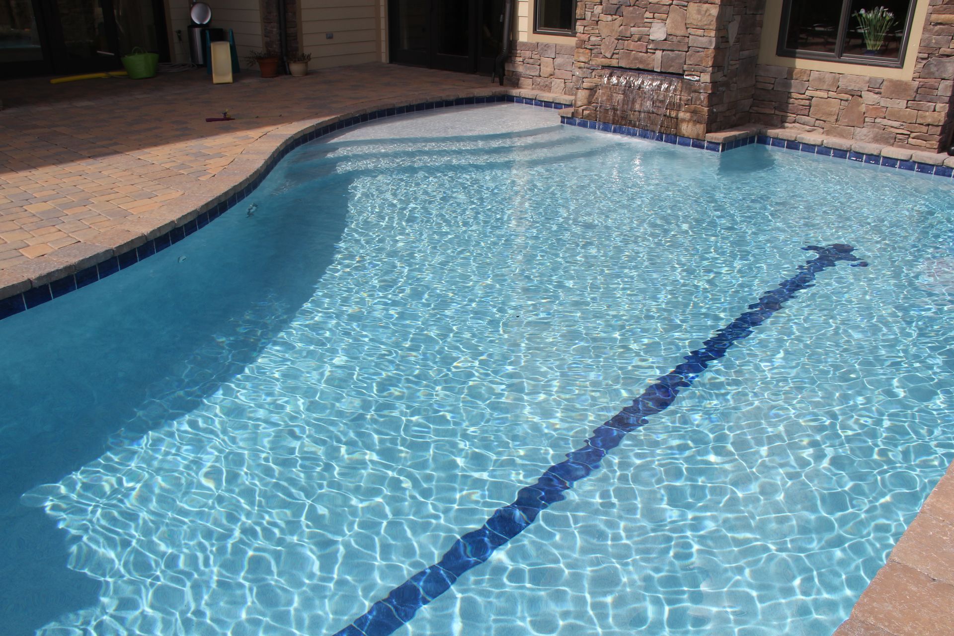 Blue backyard swimming pool with a curved edge and stone patio border