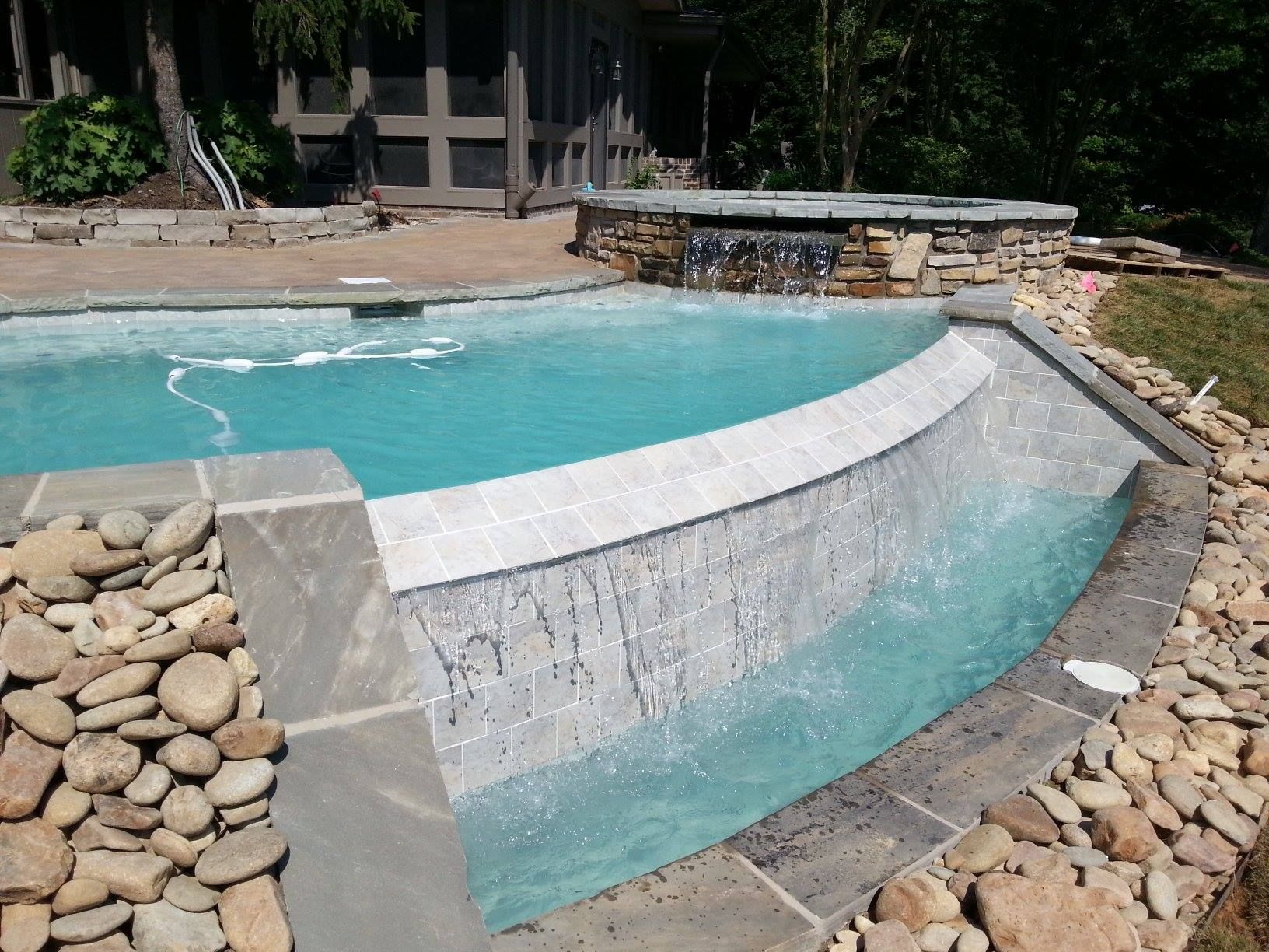 Curved backyard pool spillway with turquoise water, stone coping, and rock landscaping