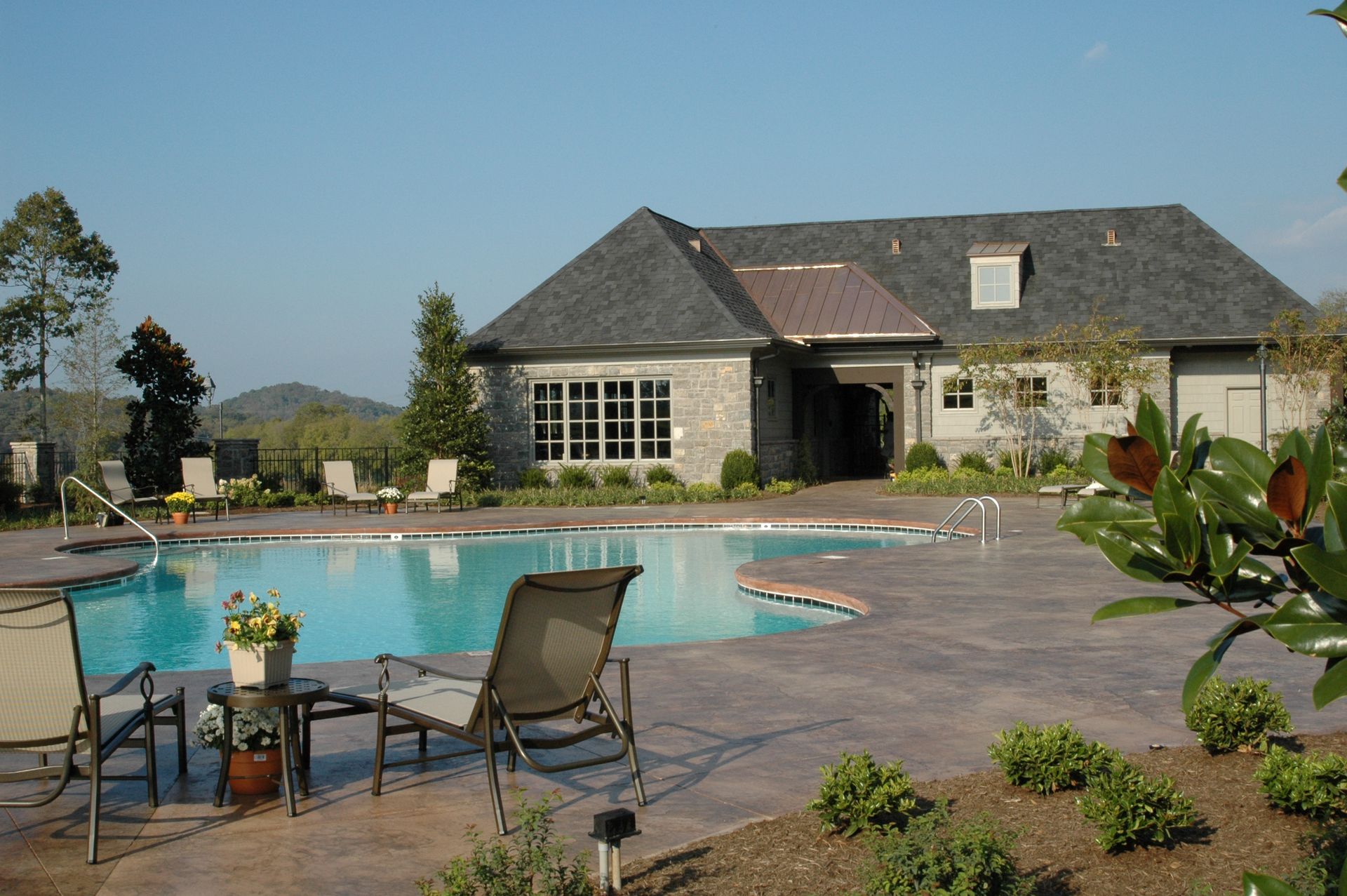 Backyard pool patio with lounge chairs and a stone house under a clear sky