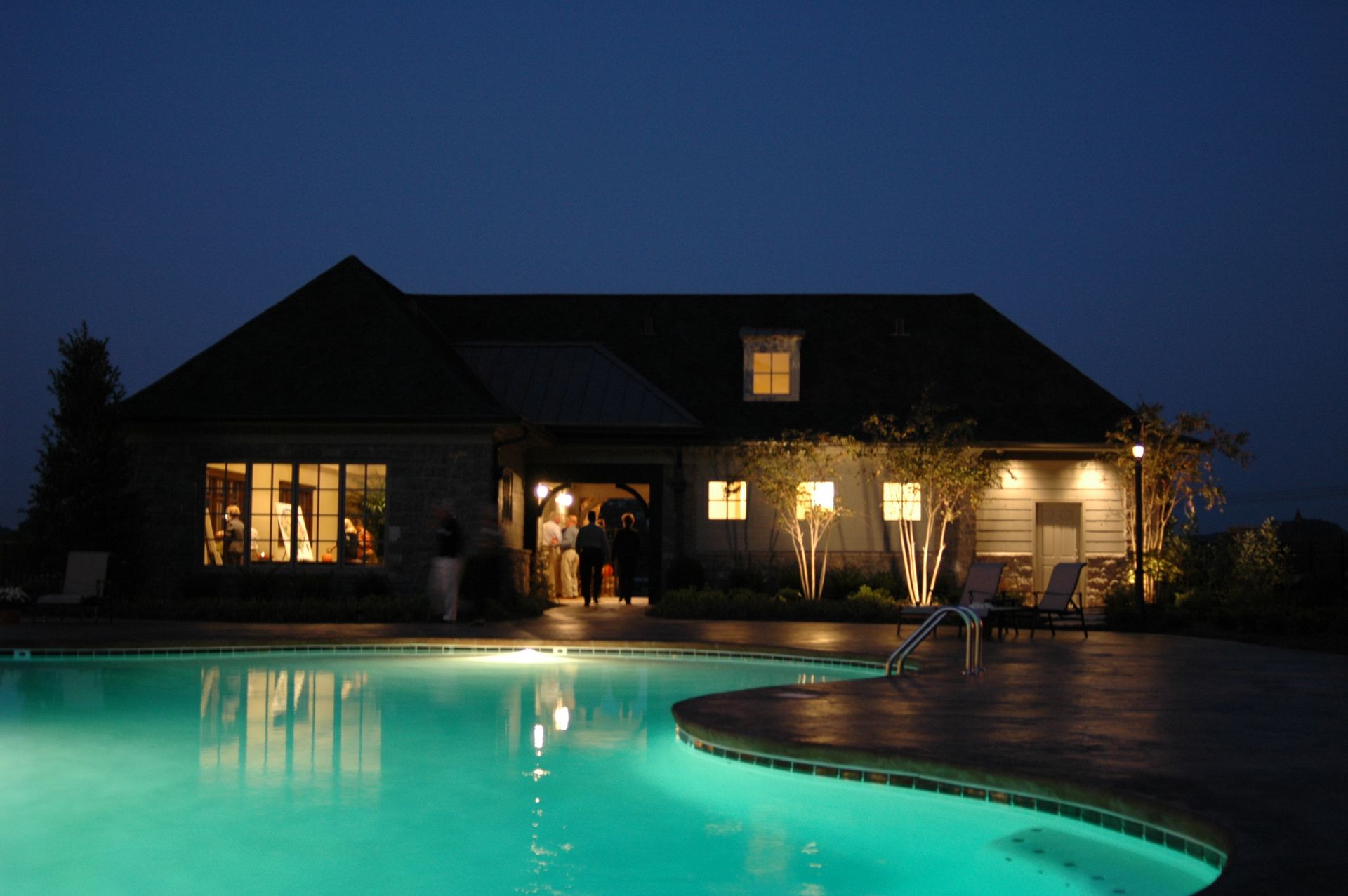 Nighttime house with lit windows and turquoise swimming pool in the foreground