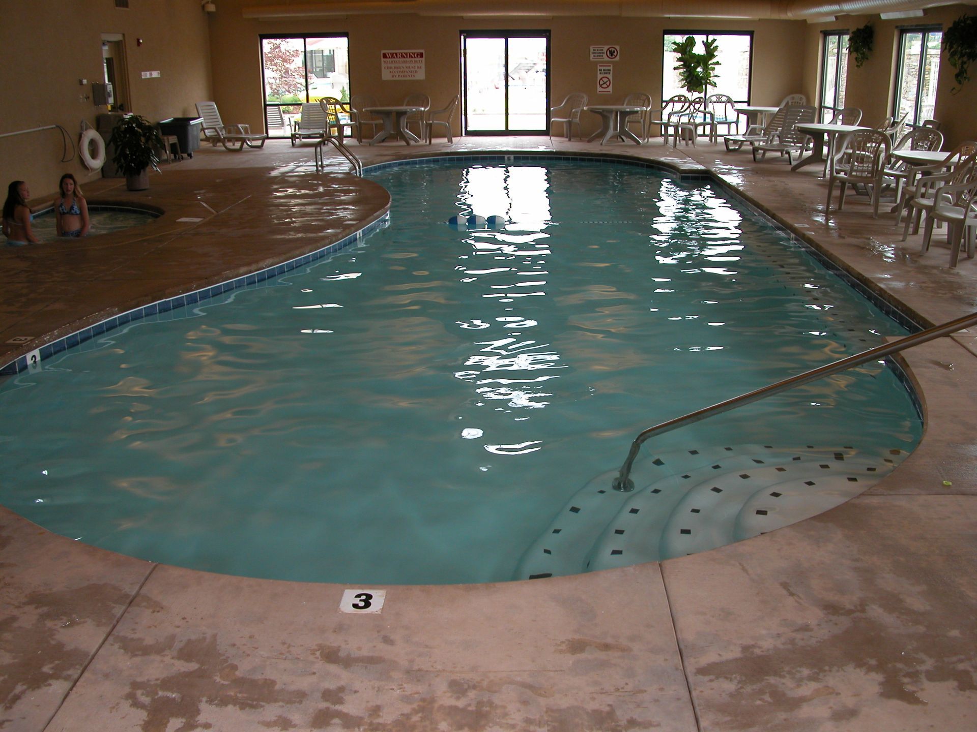 Indoor swimming pool with clear water, tiled deck, and windows along the far wall