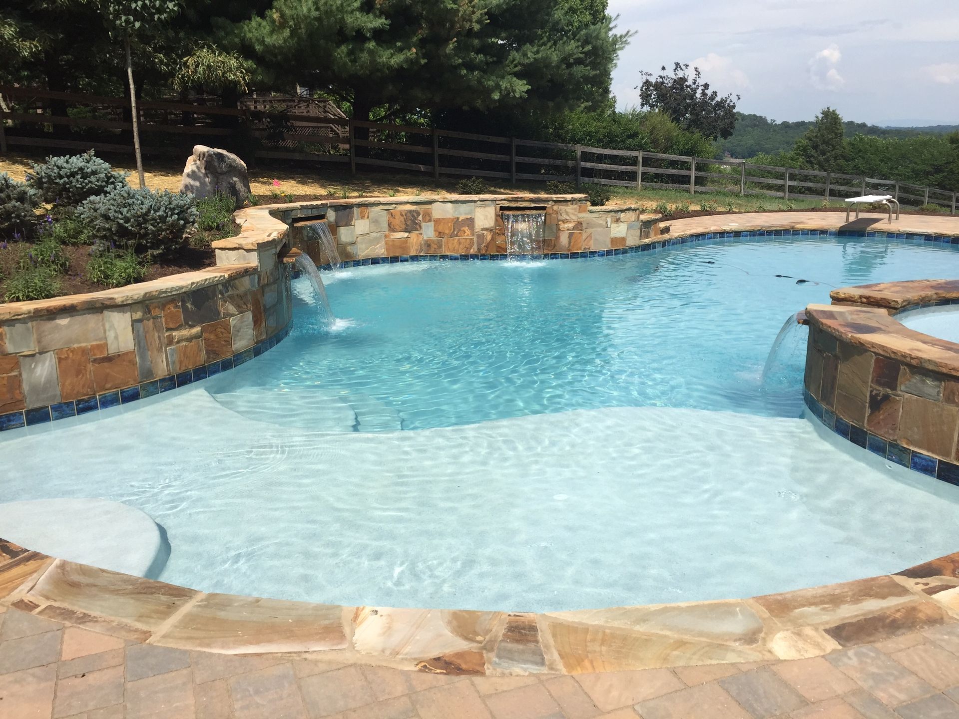 Curved backyard swimming pool with clear blue water and stone landscaping under trees