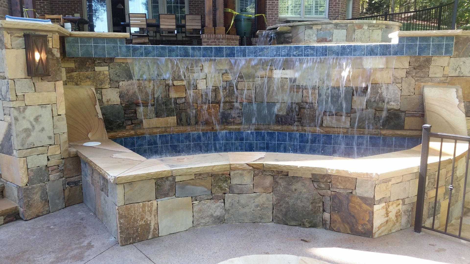 Stone water feature with a small waterfall into a tiled pool in an outdoor courtyard