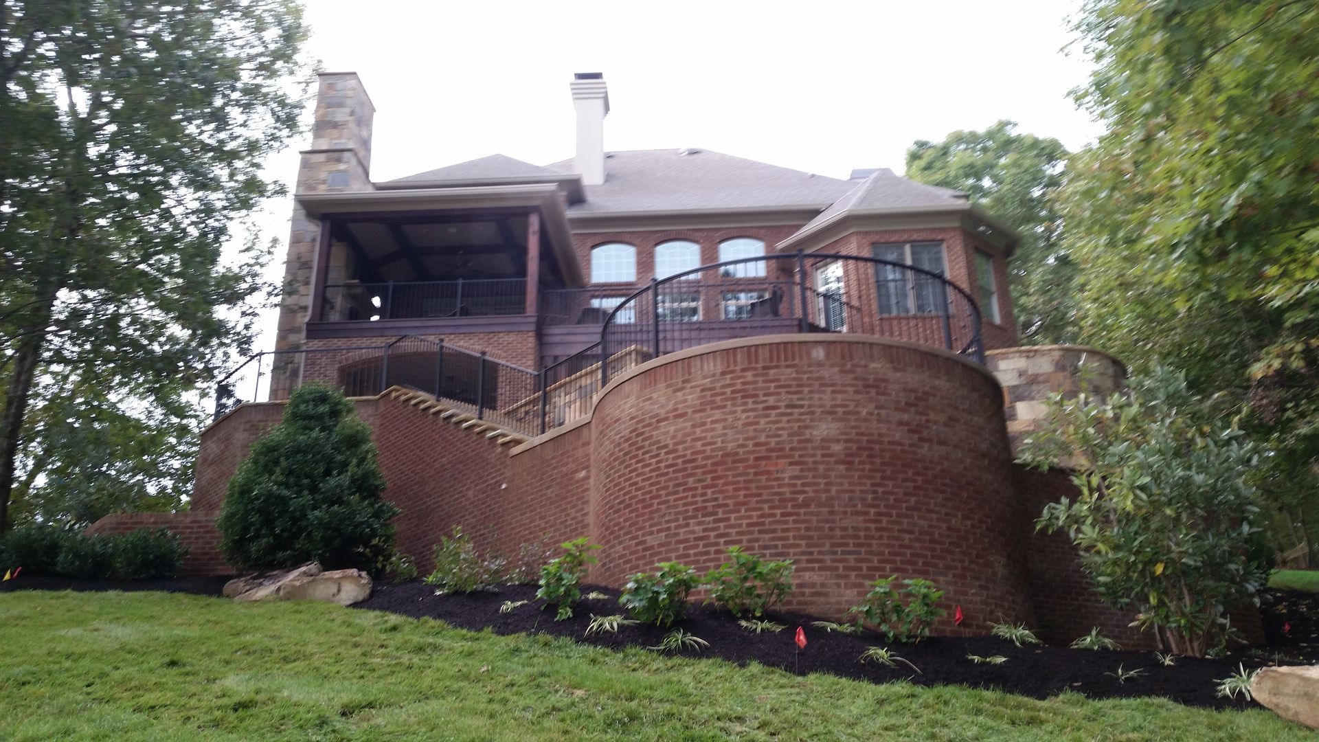 Brick house with a curved retaining wall and landscaped yard among tall trees