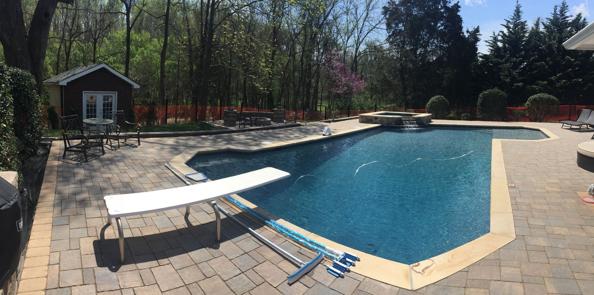 Backyard swimming pool with diving board, lounge chairs, and paver deck surrounded by trees