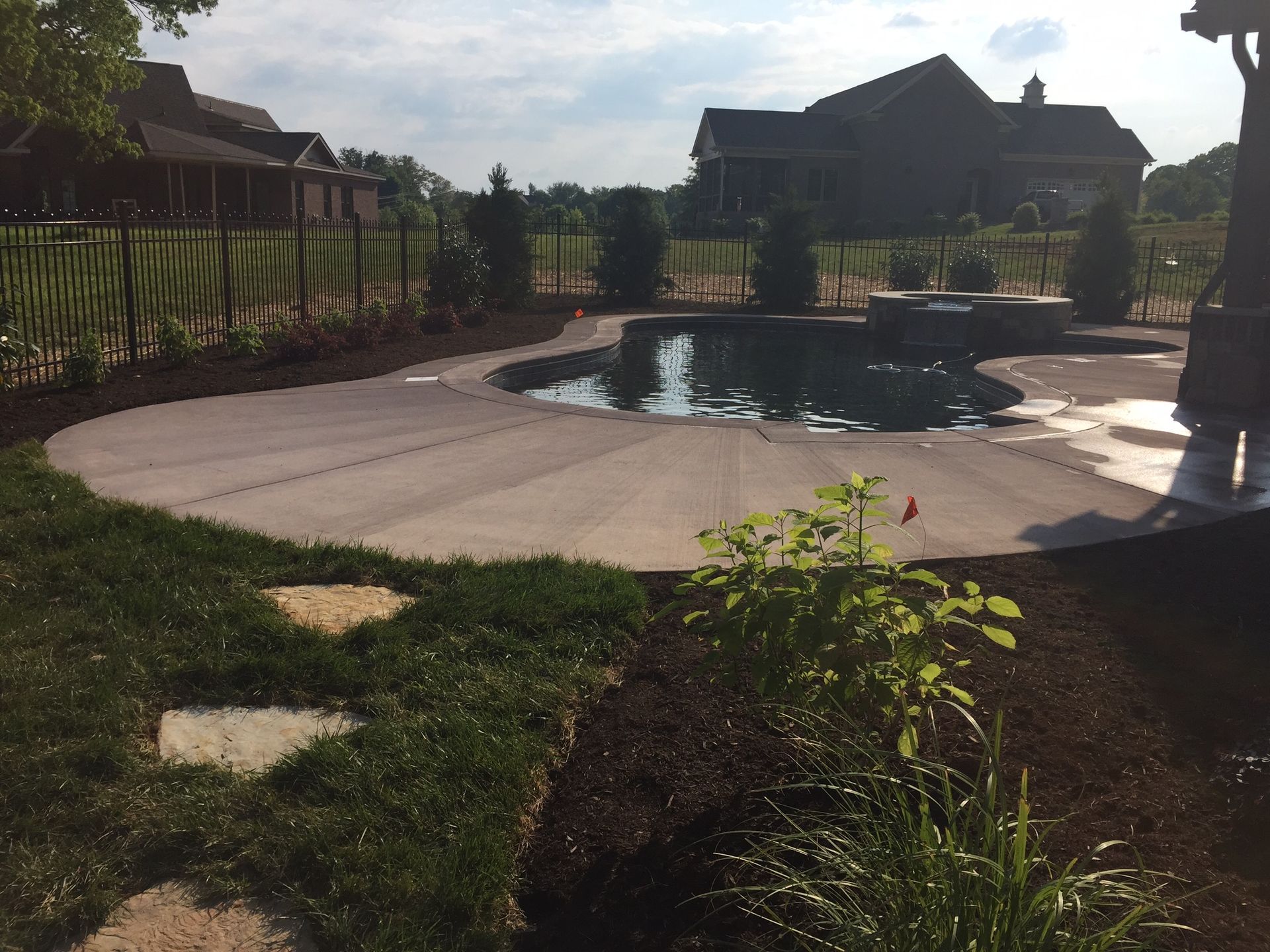 Backyard patio with a small pool, curved concrete path, grass, and houses in the background