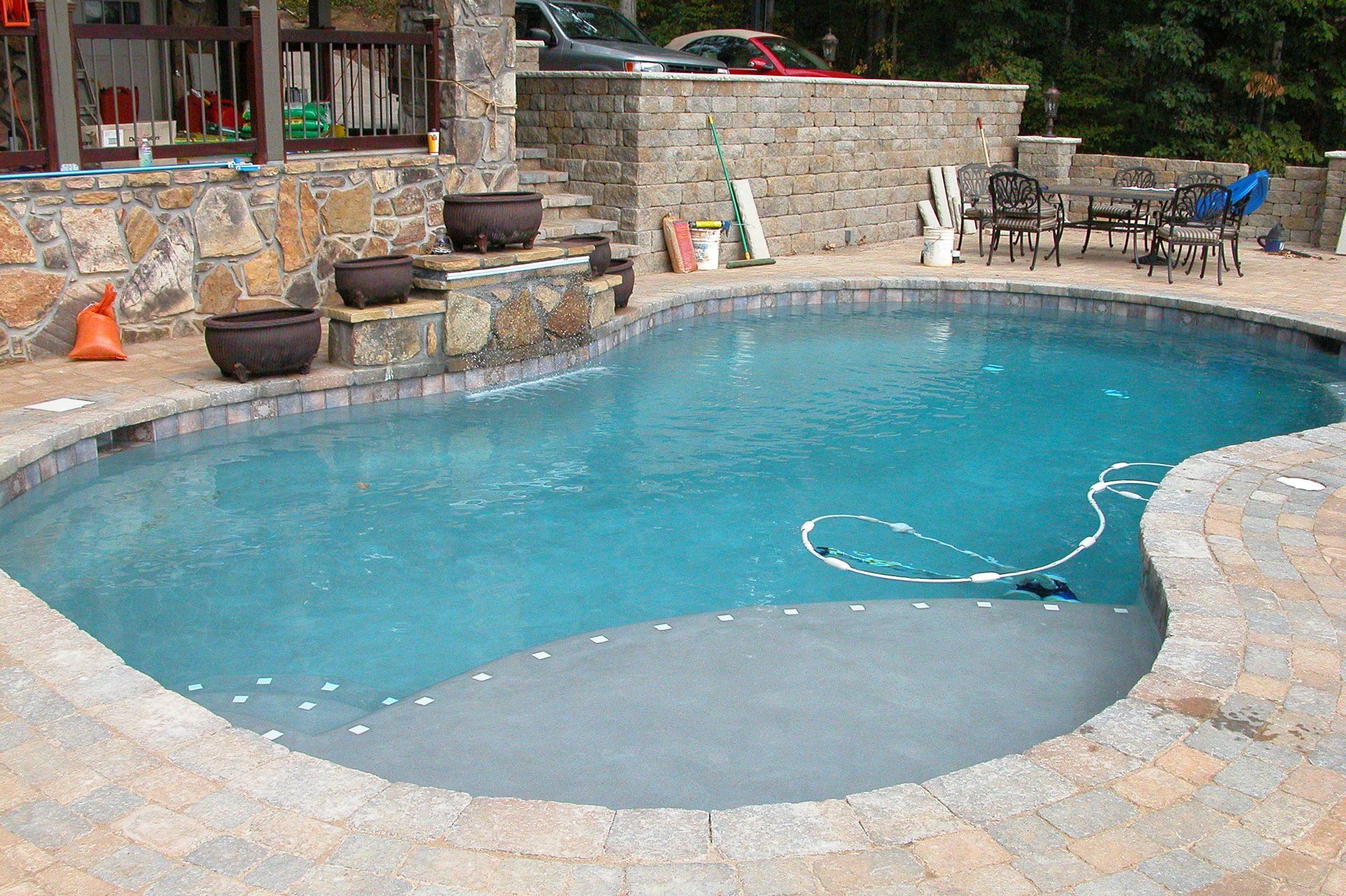 Stone backyard pool with turquoise water and a built-in hot tub area surrounded by patio seating
