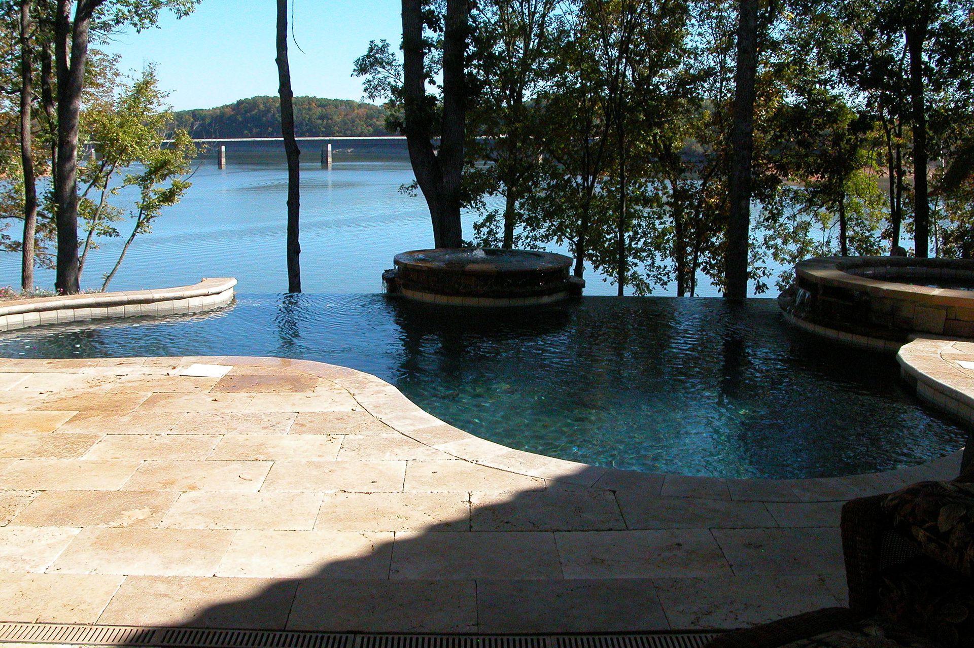 Shaded poolside deck overlooking a calm blue lake with trees and docks in the distance
