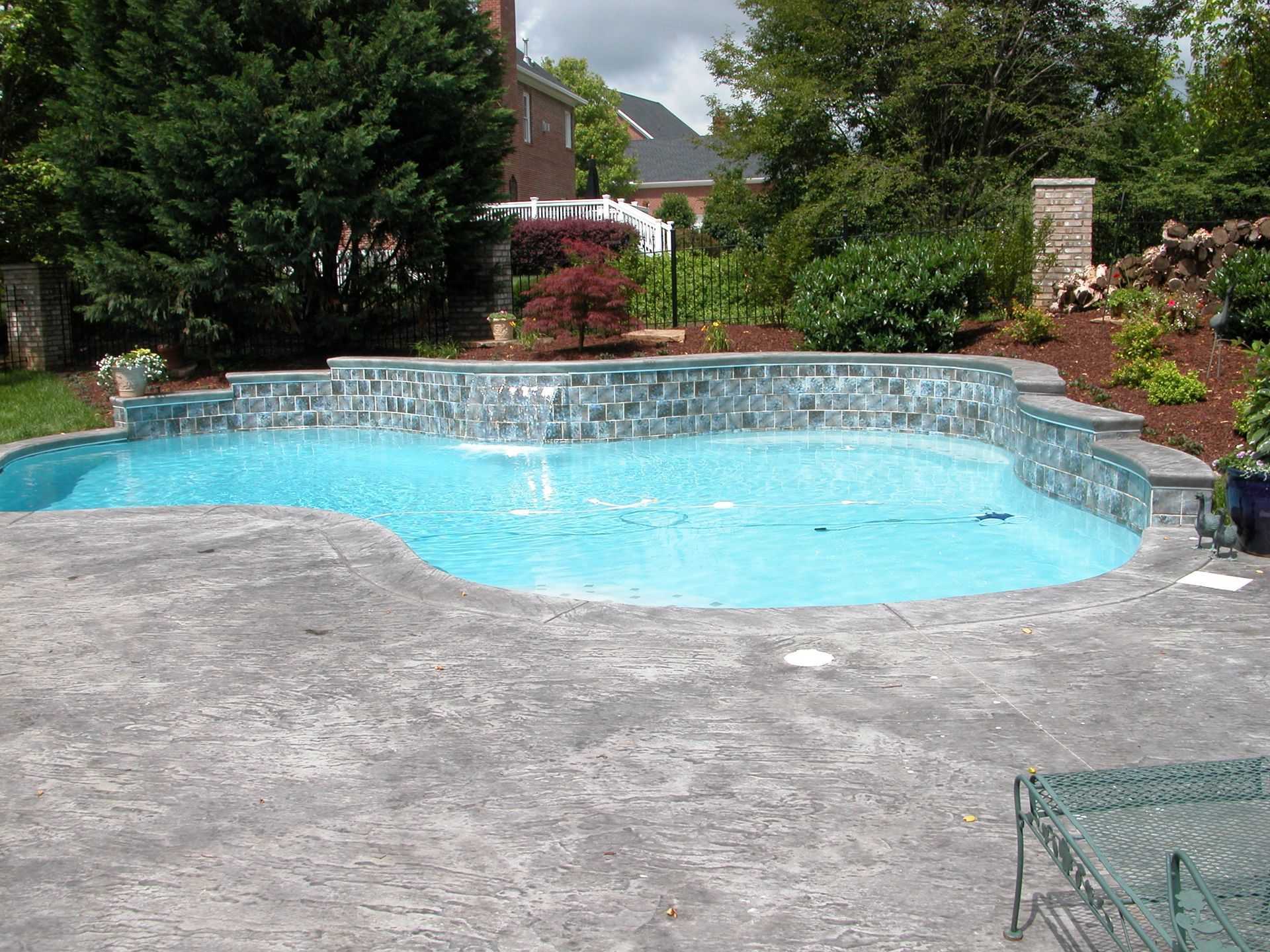 Backyard swimming pool with blue water, stone deck, and surrounding greenery