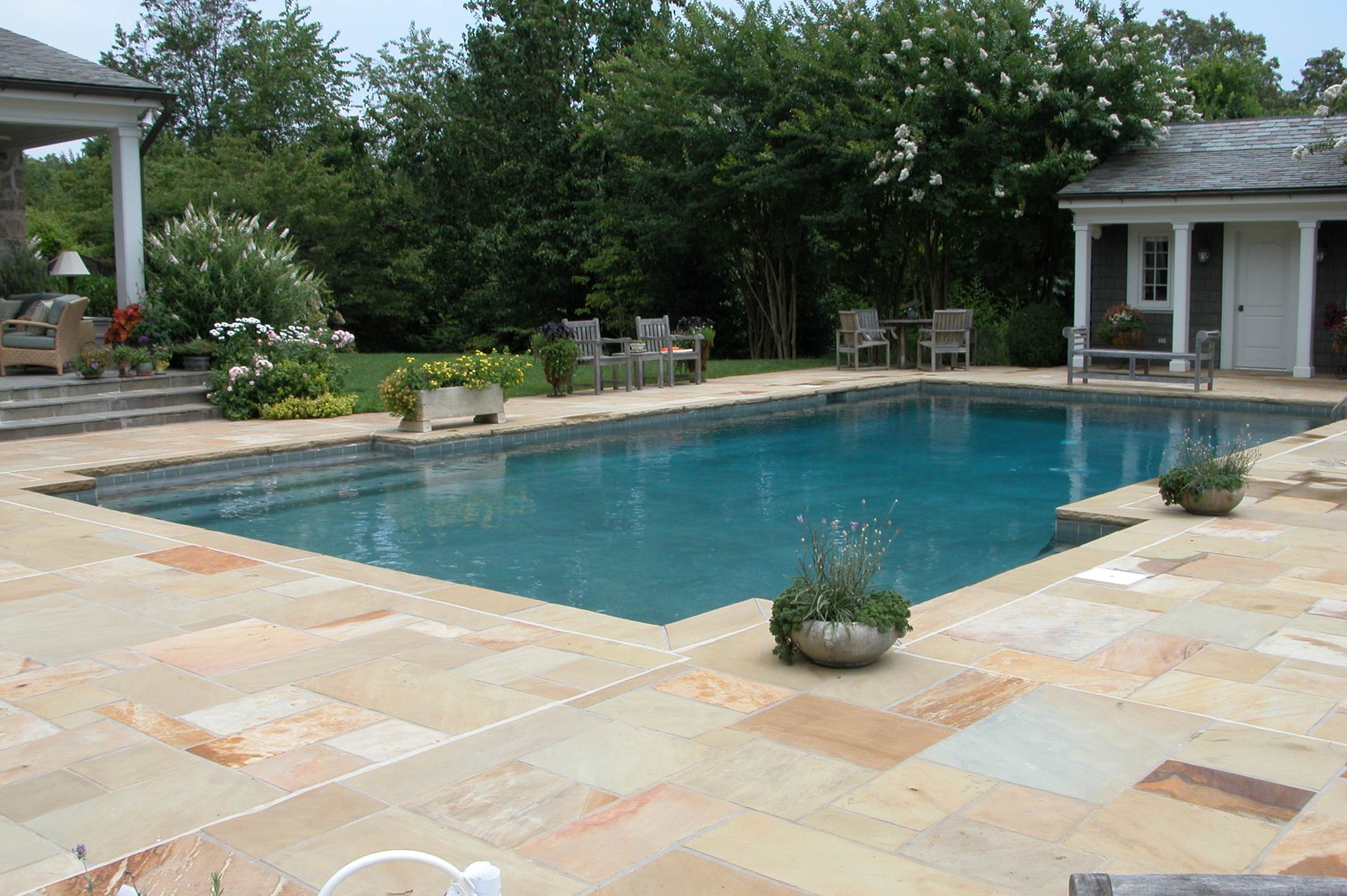Backyard swimming pool with stone patio, lounge chairs, and lush greenery