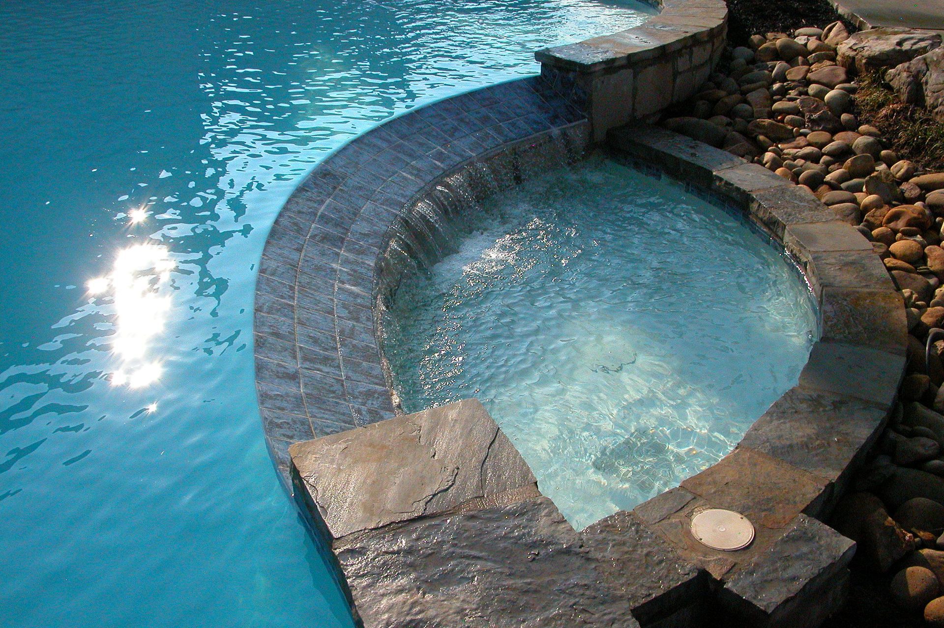 Curved stone pool with clear blue water beside a larger swimming pool