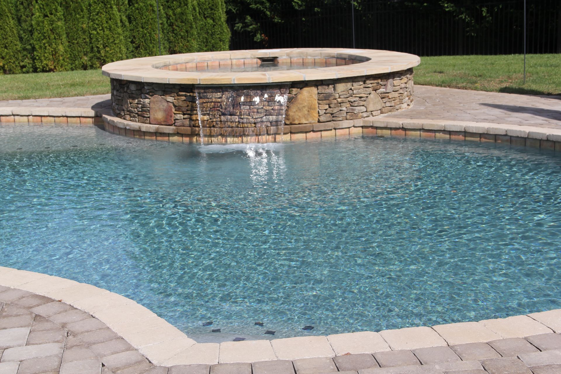 Outdoor swimming pool with a raised stone water feature and light gray paver deck