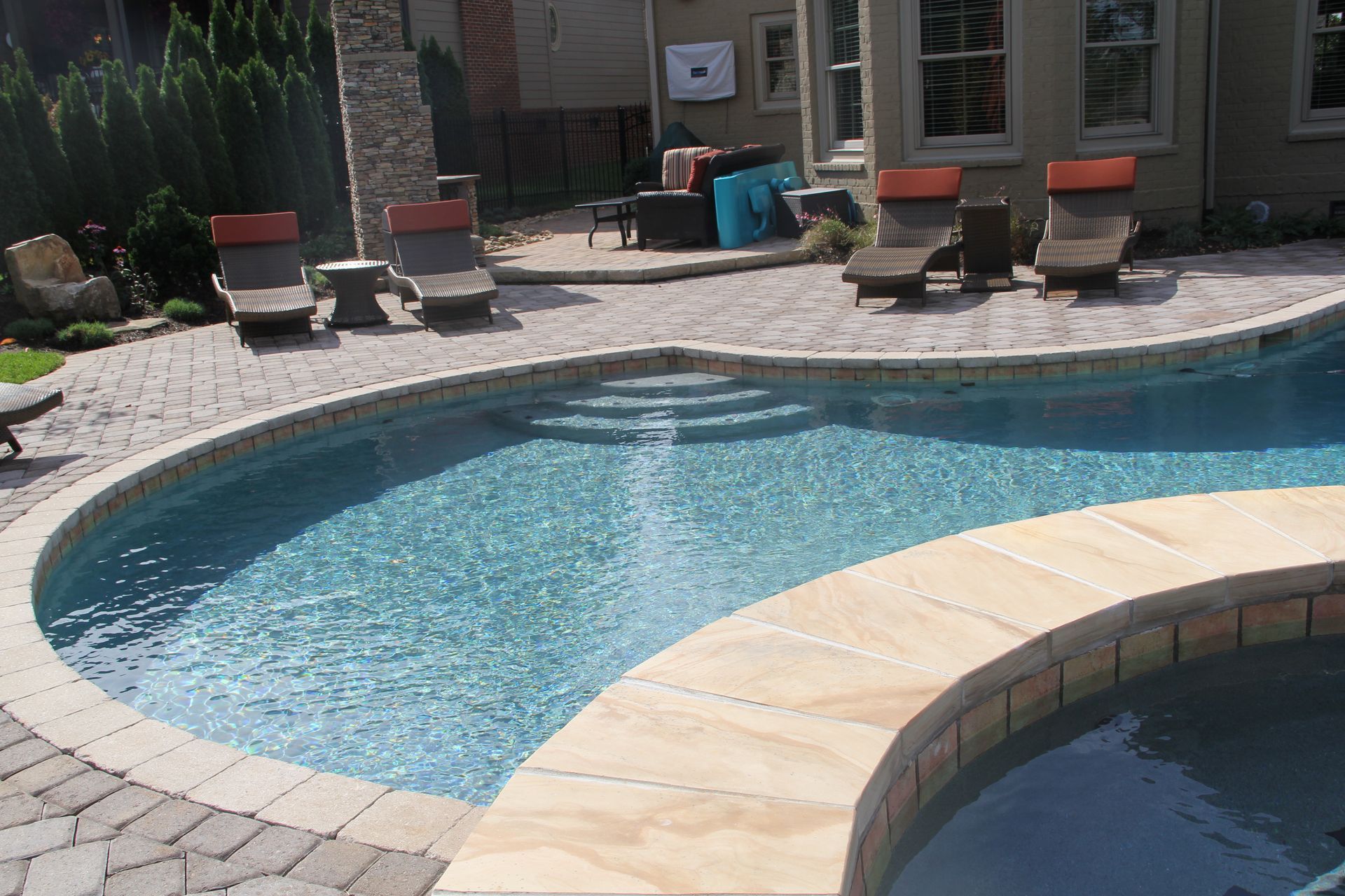 Backyard swimming pool with lounge chairs and a curved stone edge, viewed from the patio