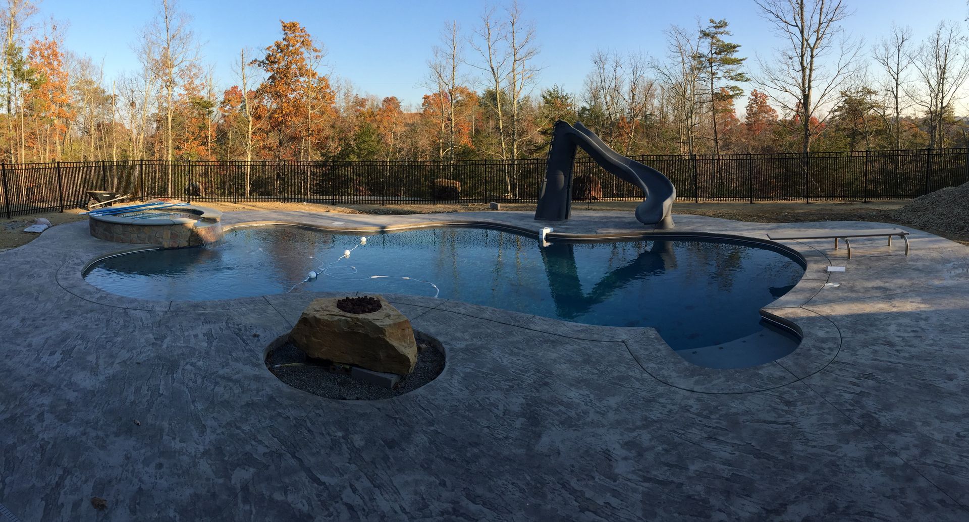 Frozen pond with a dark hole, a pump, and trees along the shore at sunset