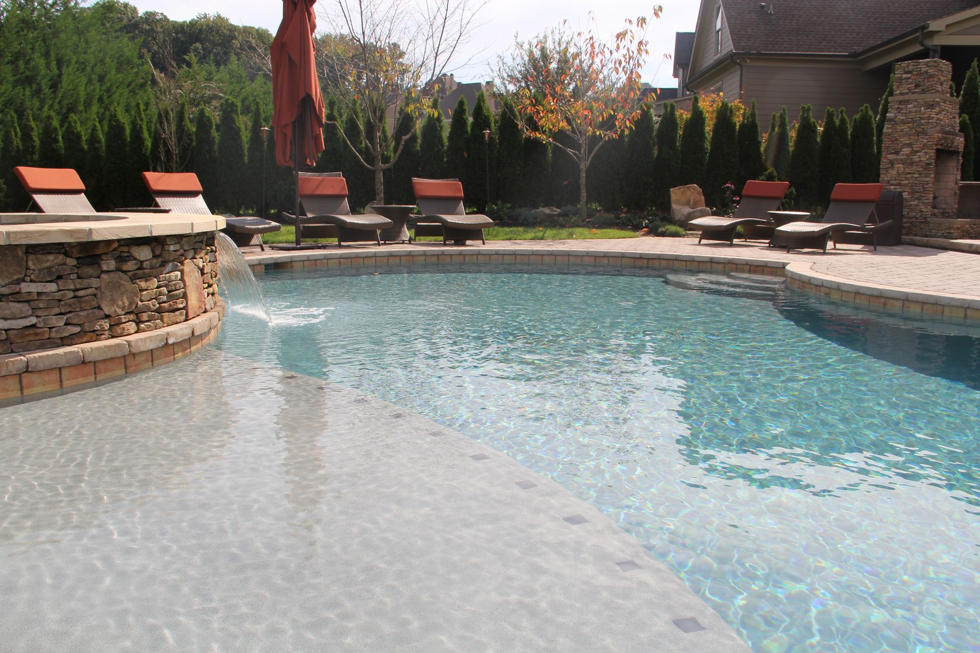 Backyard swimming pool with lounge chairs, stone patio, and trees in the background