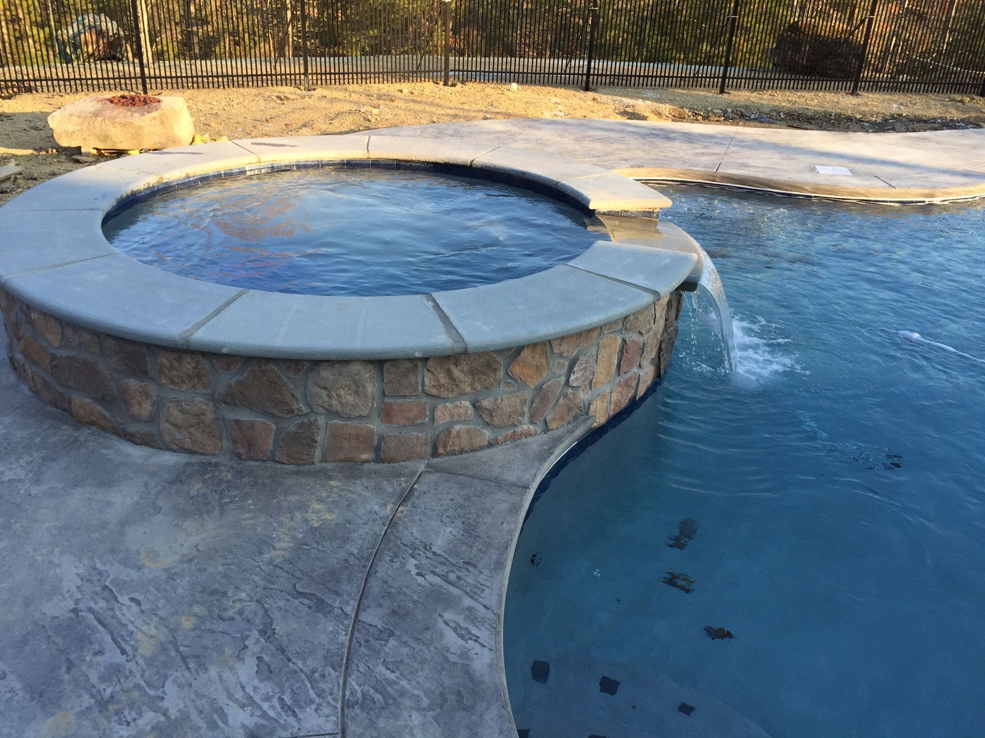 Stone hot tub beside a blue swimming pool in a sunny backyard