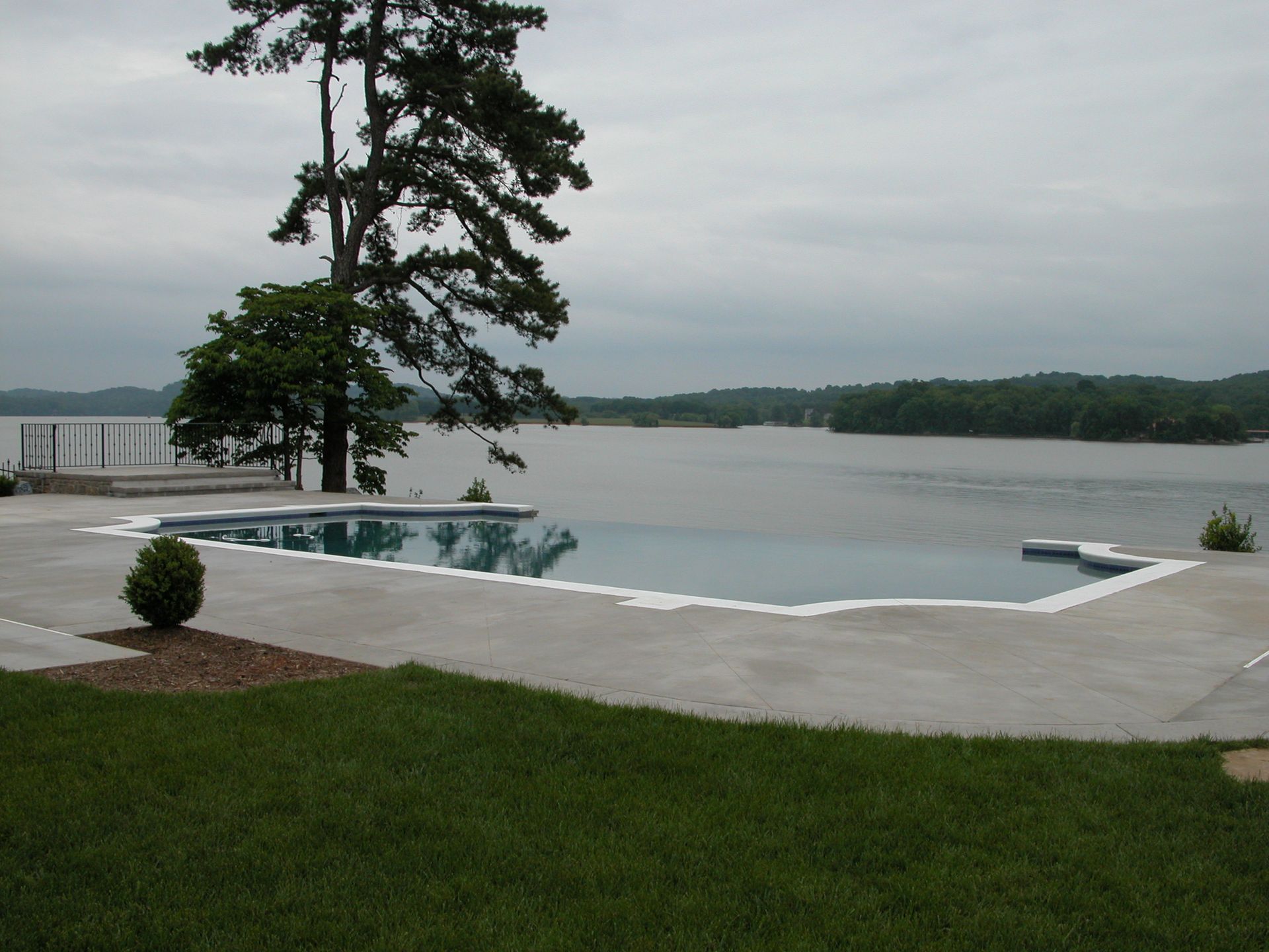 Infinity pool overlooking a calm lake, with tall pine trees and cloudy sky.