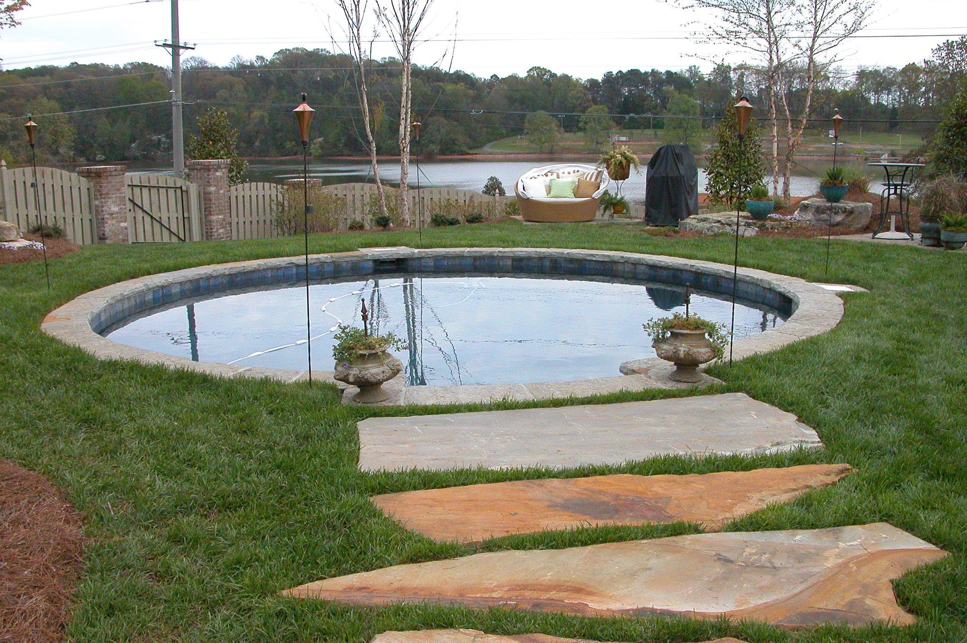 Backyard pond with stepping stones, grass, and a fenced yard in the background