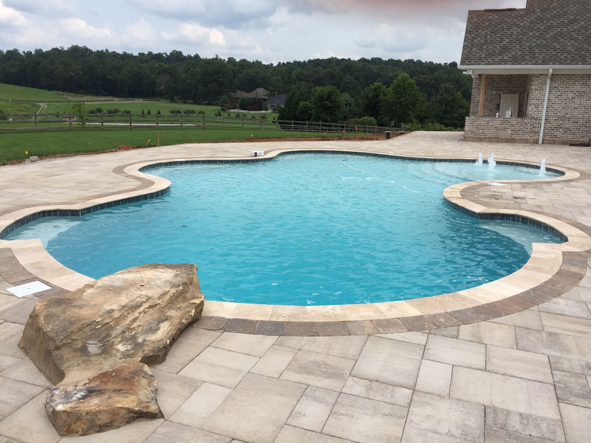 Backyard swimming pool with tan stone deck and a grassy landscape beyond